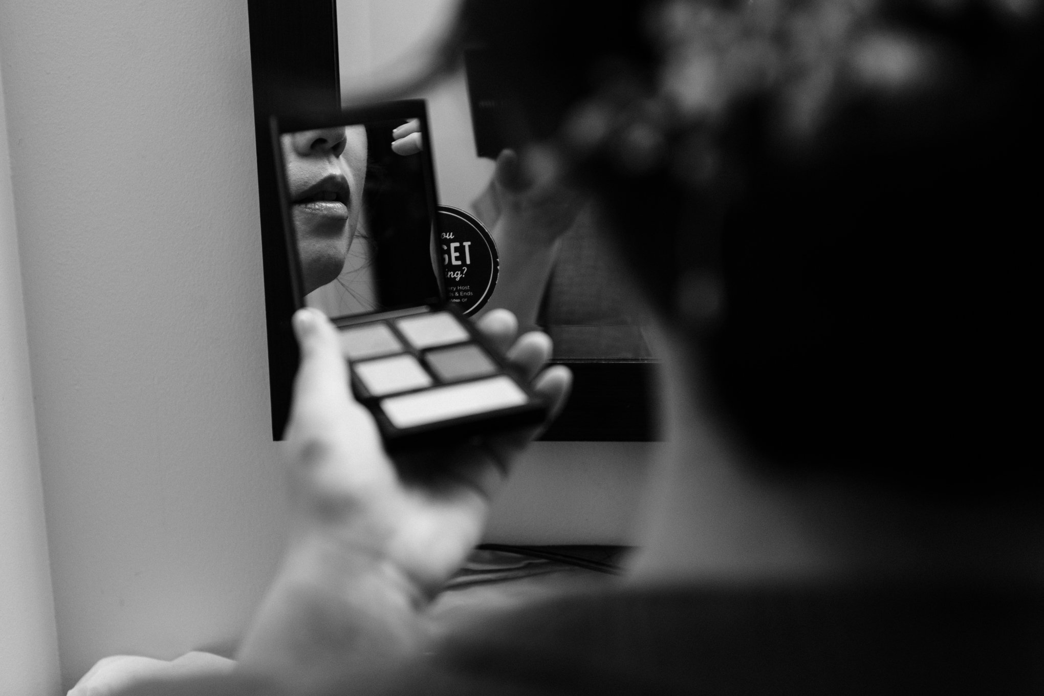 A person holding a compact mirror and makeup palette, looking at their reflection, with focus on lips and face in the mirror.