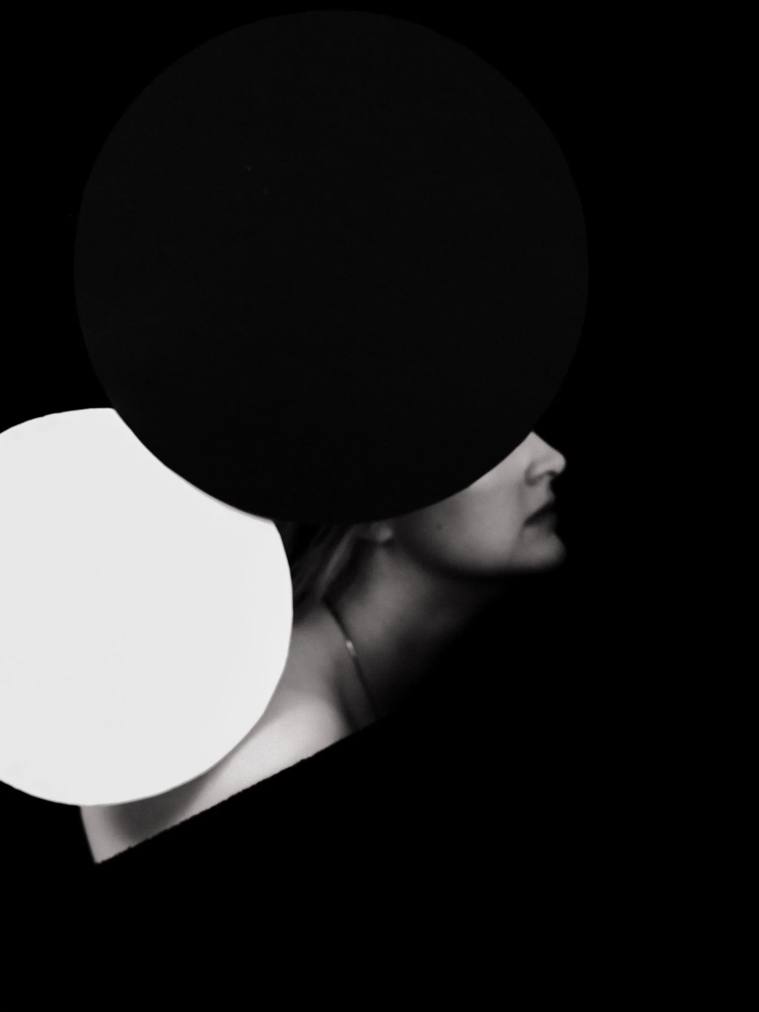 Black and white photo of a woman's face turned in profile, with large black and white circular shapes obscuring parts of her face and head.
