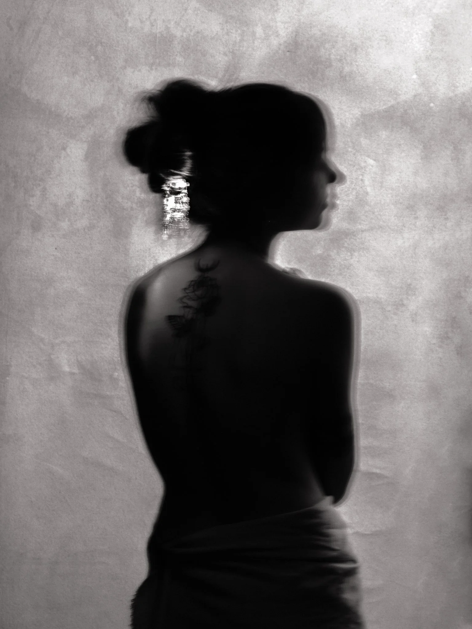 Silhouette of a woman with her hair in a bun, facing to the right, in front of a textured wall.