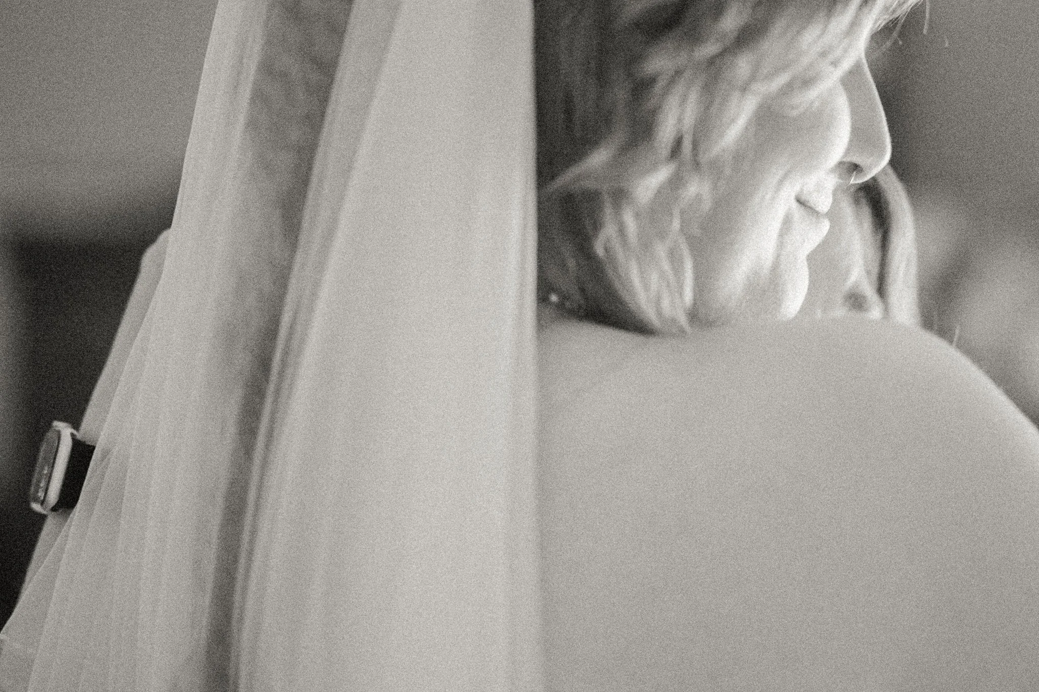 Black and white photograph of a woman with wavy hair, smiling softly, as she leans over a surface, possibly a table or counter.