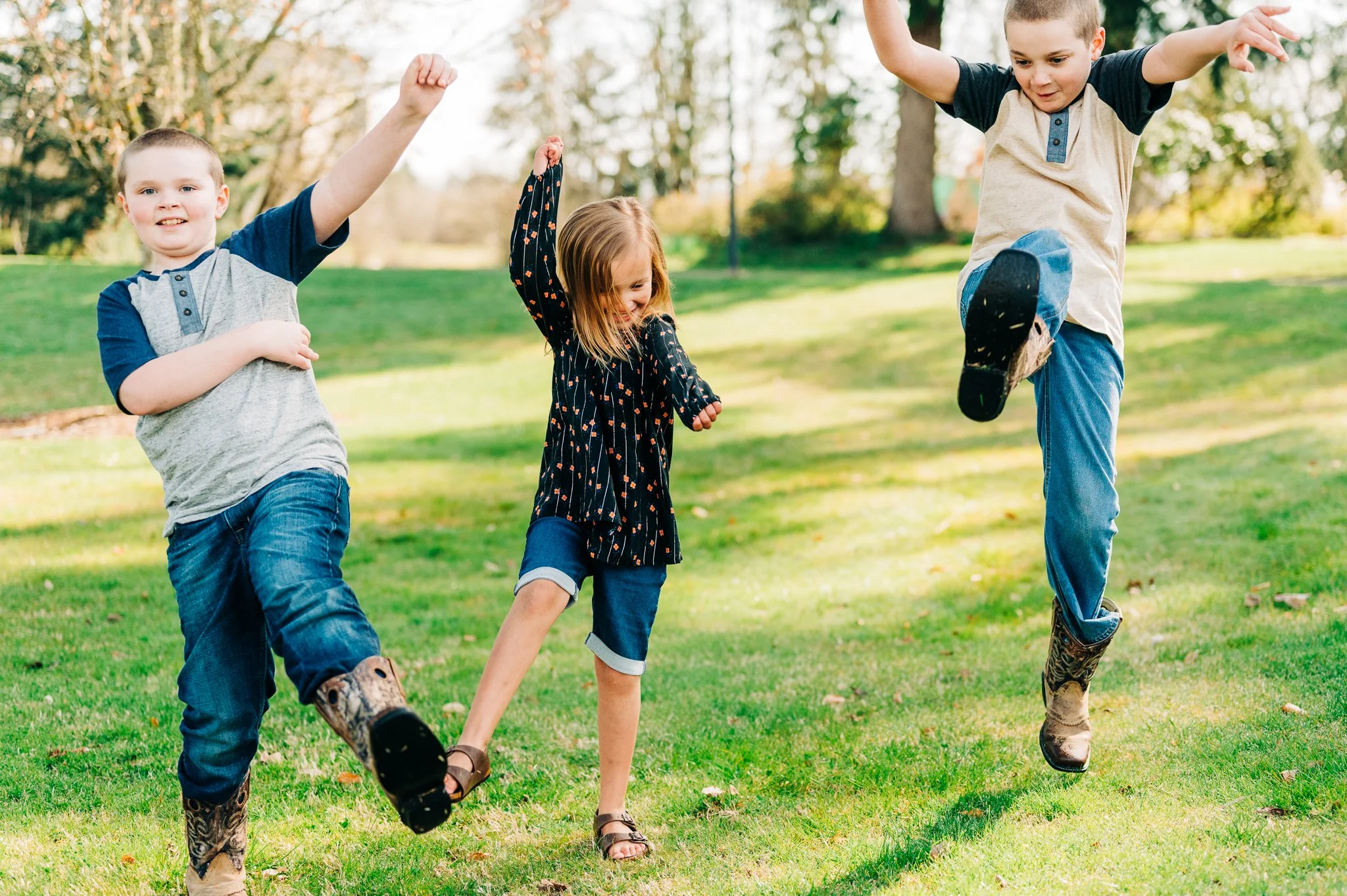 Three children playing and jumping on a grassy field in a park during daytime.