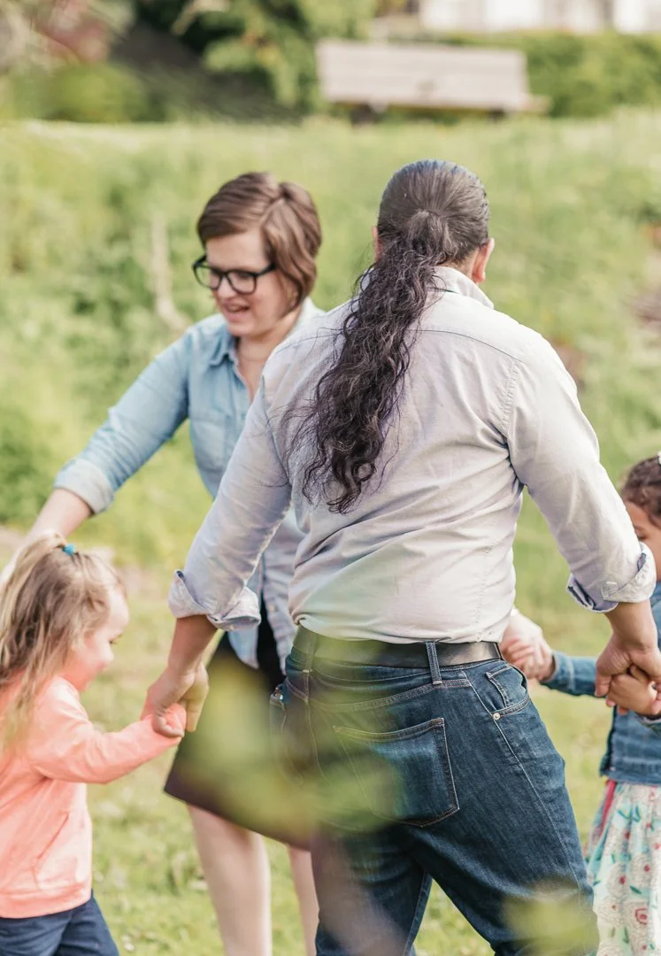 Adults and children holding hands and playing in a park.