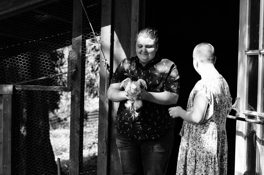 Two young girls standing near a wooden animal enclosure. One girl, holding a small puppy, is smiling, and the other girl is looking away from the camera.
