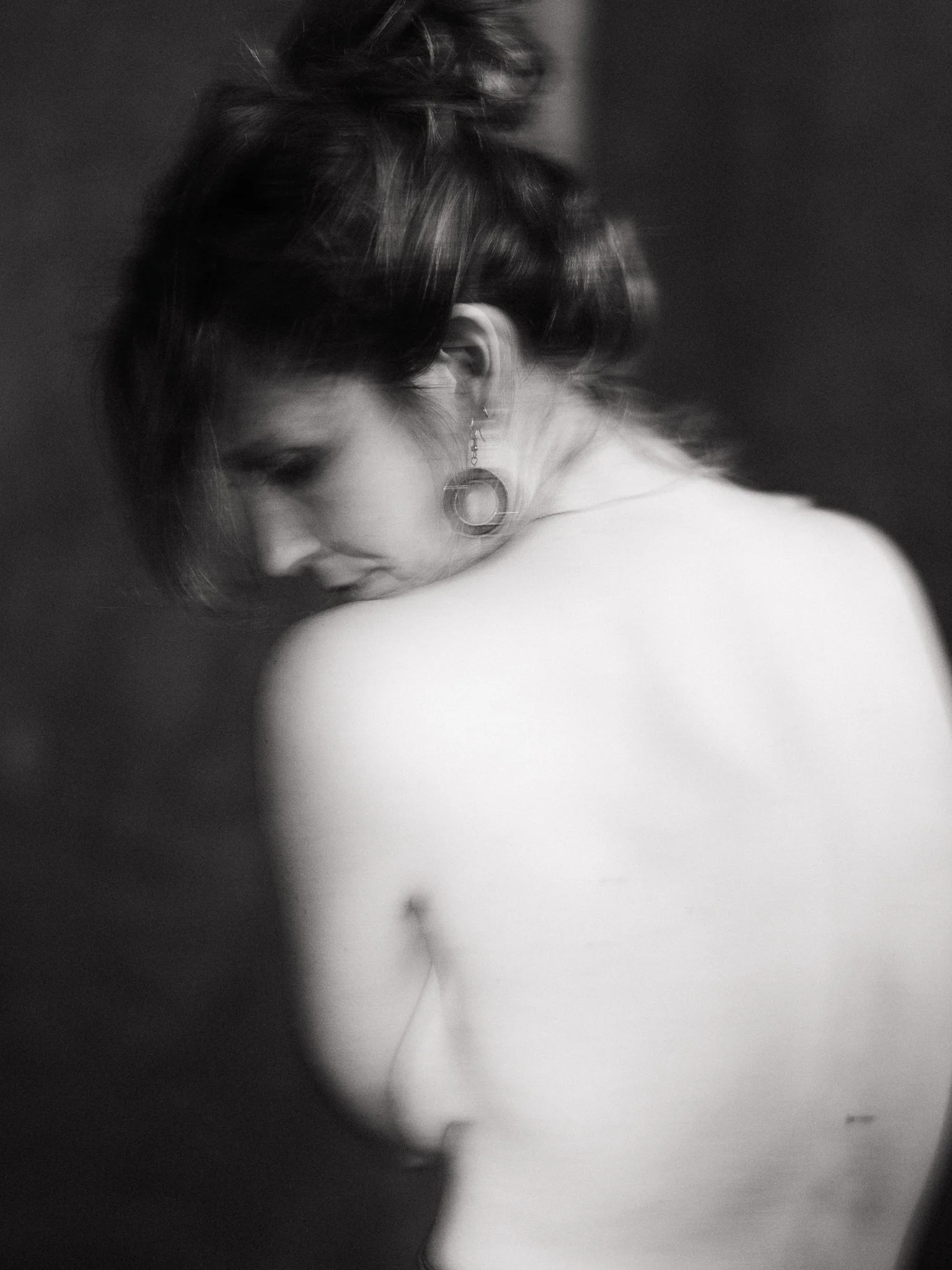 Black and white photo of a woman with short hair and earrings, looking downward with her shoulder exposed.