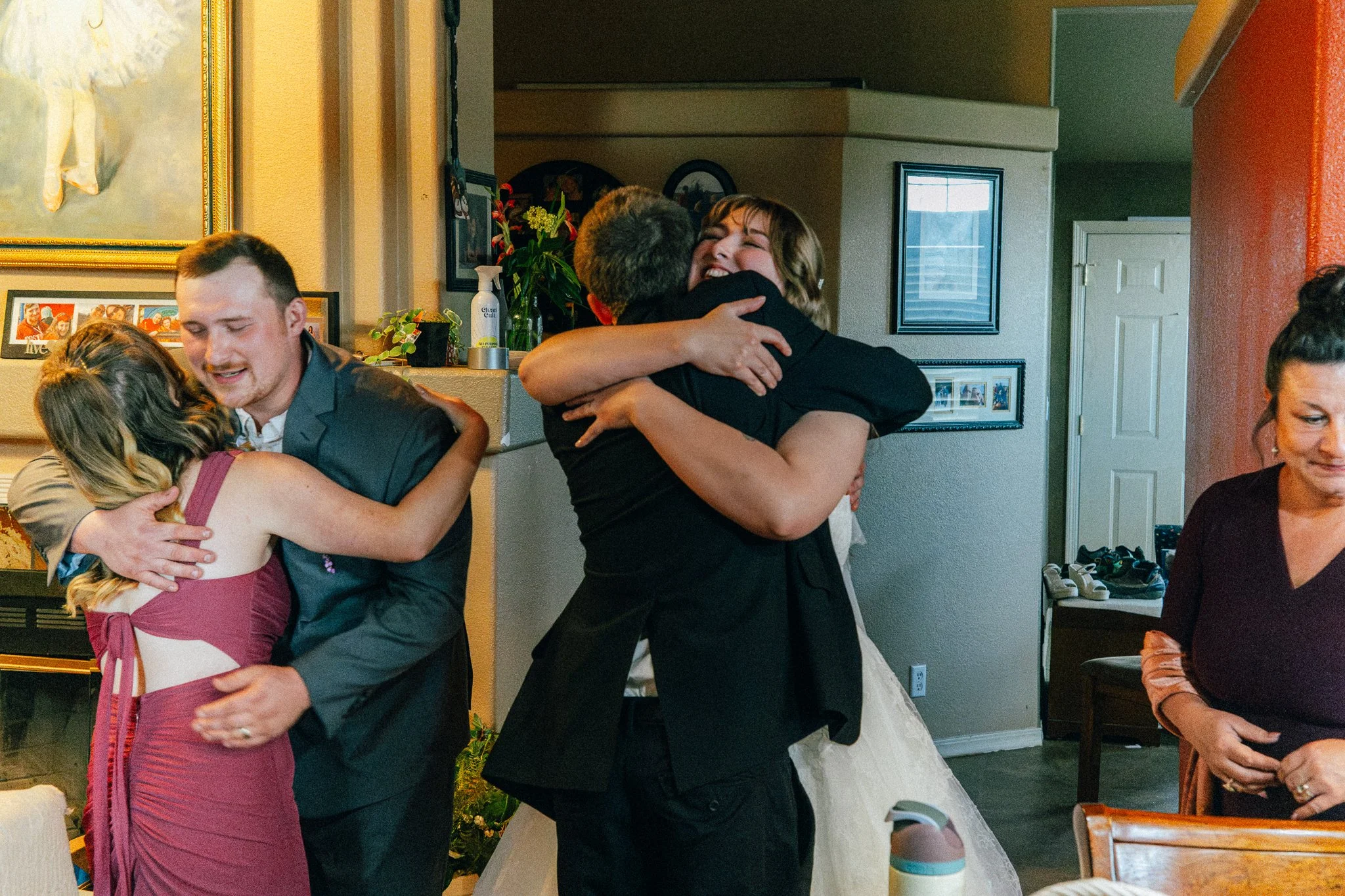 People hugging at a family gathering or celebration in a home, with some women wearing dresses and a man in a suit.