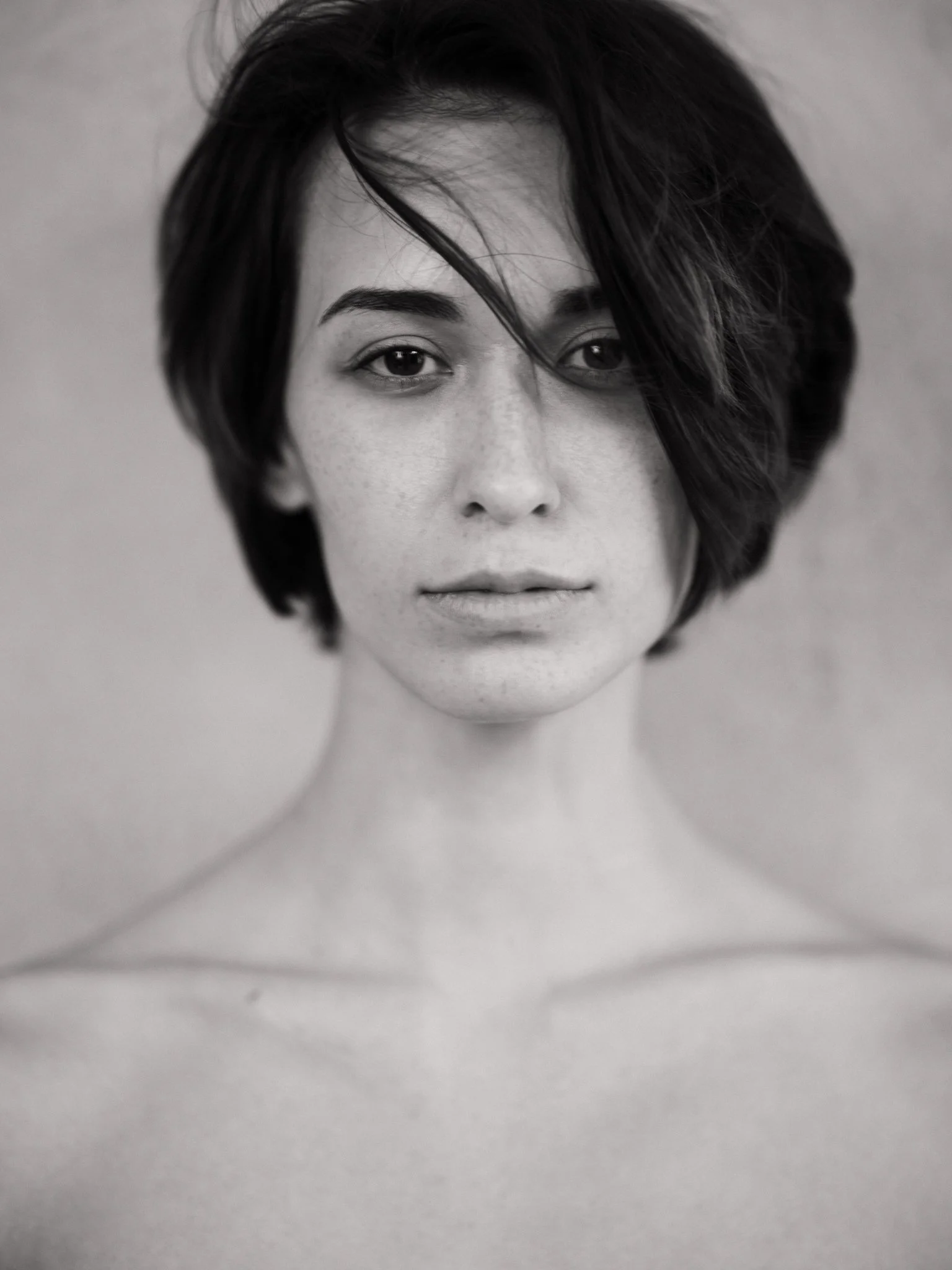 A black and white close-up portrait of a young woman with short, tousled hair and freckles, looking directly at the camera.