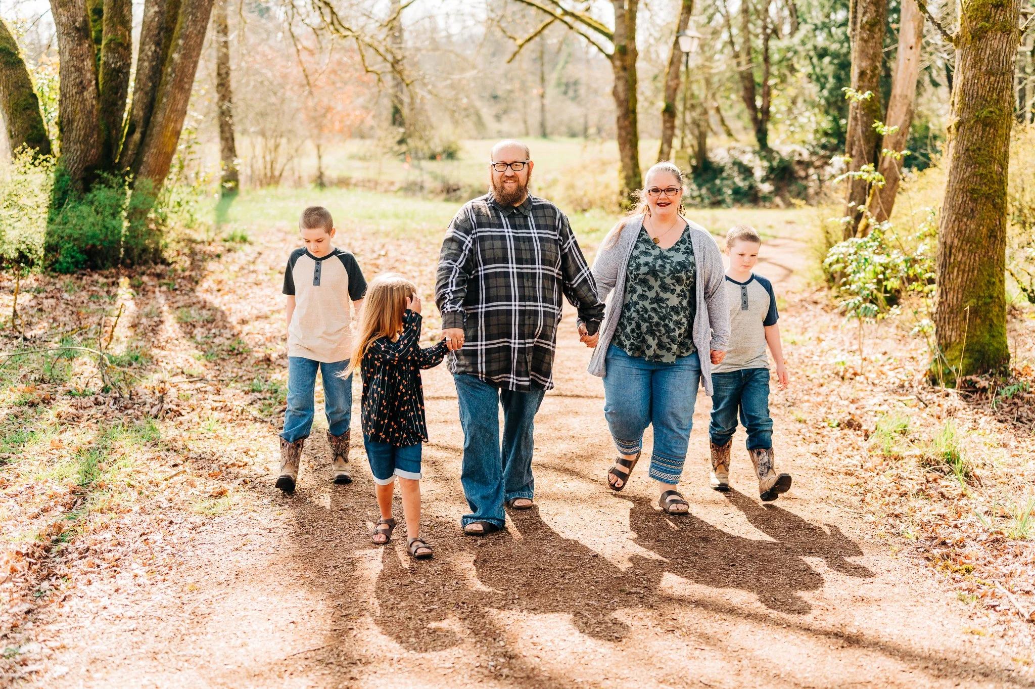 A family of six walking hand-in-hand on a dirt path through a wooded park during fall.