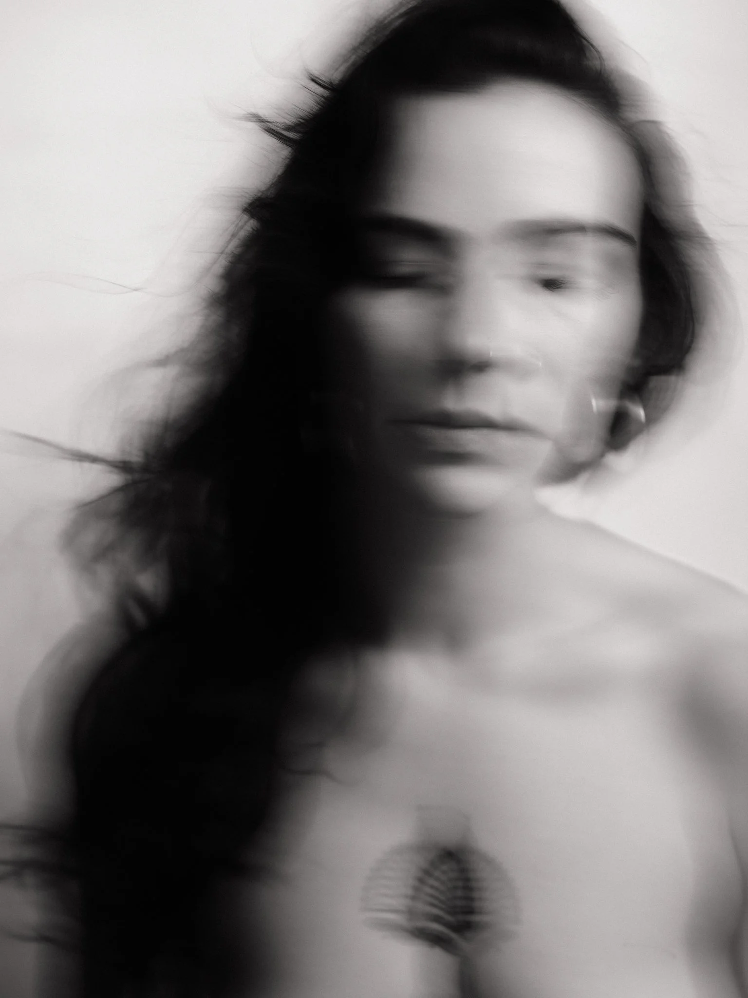 Black and white blurry photo of a woman with long hair, one eye winking, wearing earrings and a top with a striped pattern on the chest.