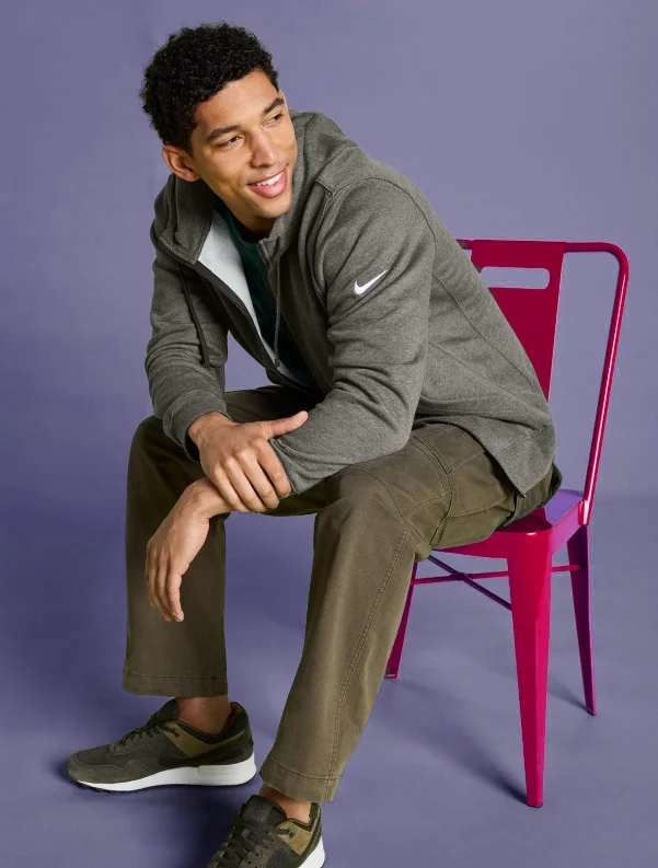 Yound man sitting on Red chair with grey Jacket with Nike logo on Left Sleeve