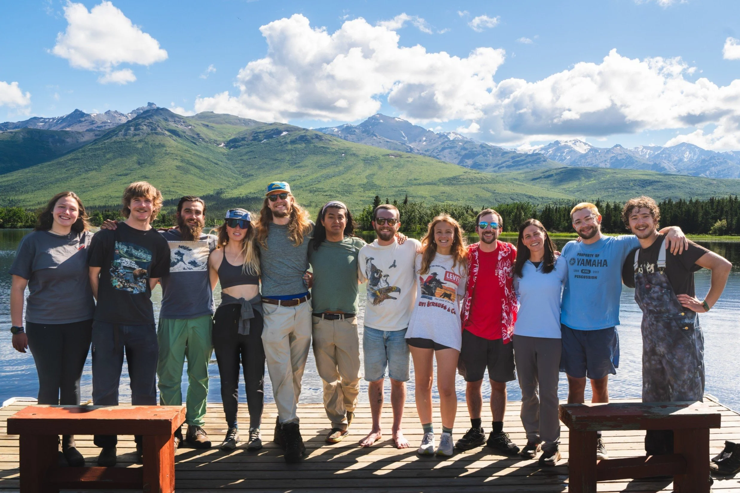 Group of people standing on a dock with mountains and a lake in the background during daytime.