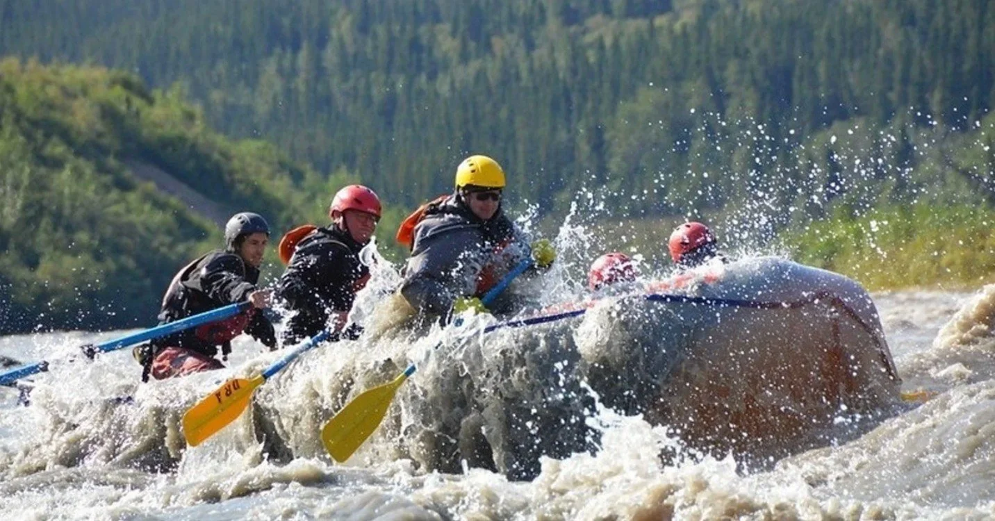 A group of five people wearing helmets and life jackets white-water rafting on a river.