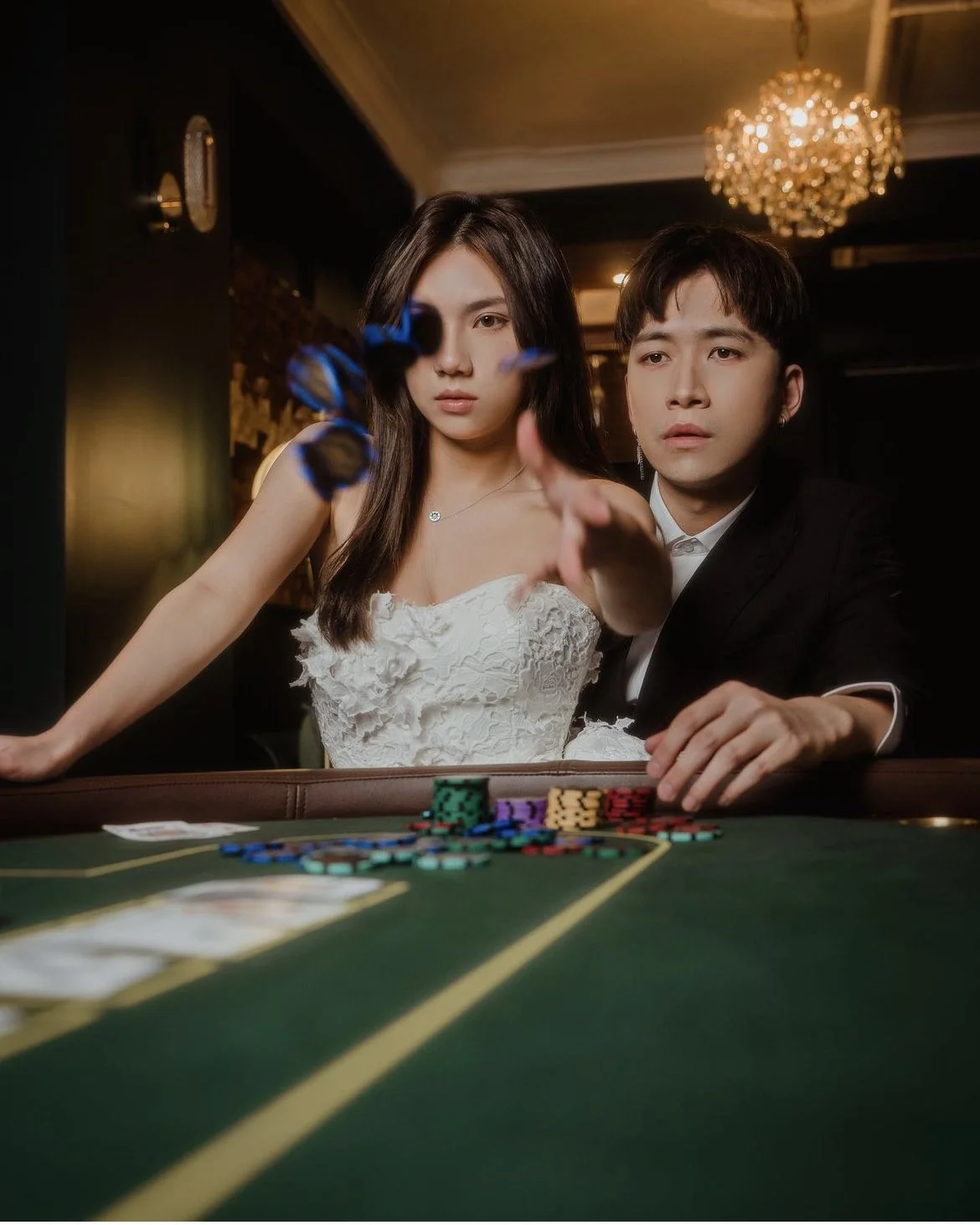 Young woman and man enjoying a casino game at a card table with poker chips, the woman in a white dress and the man in a black suit, both focused on the game.