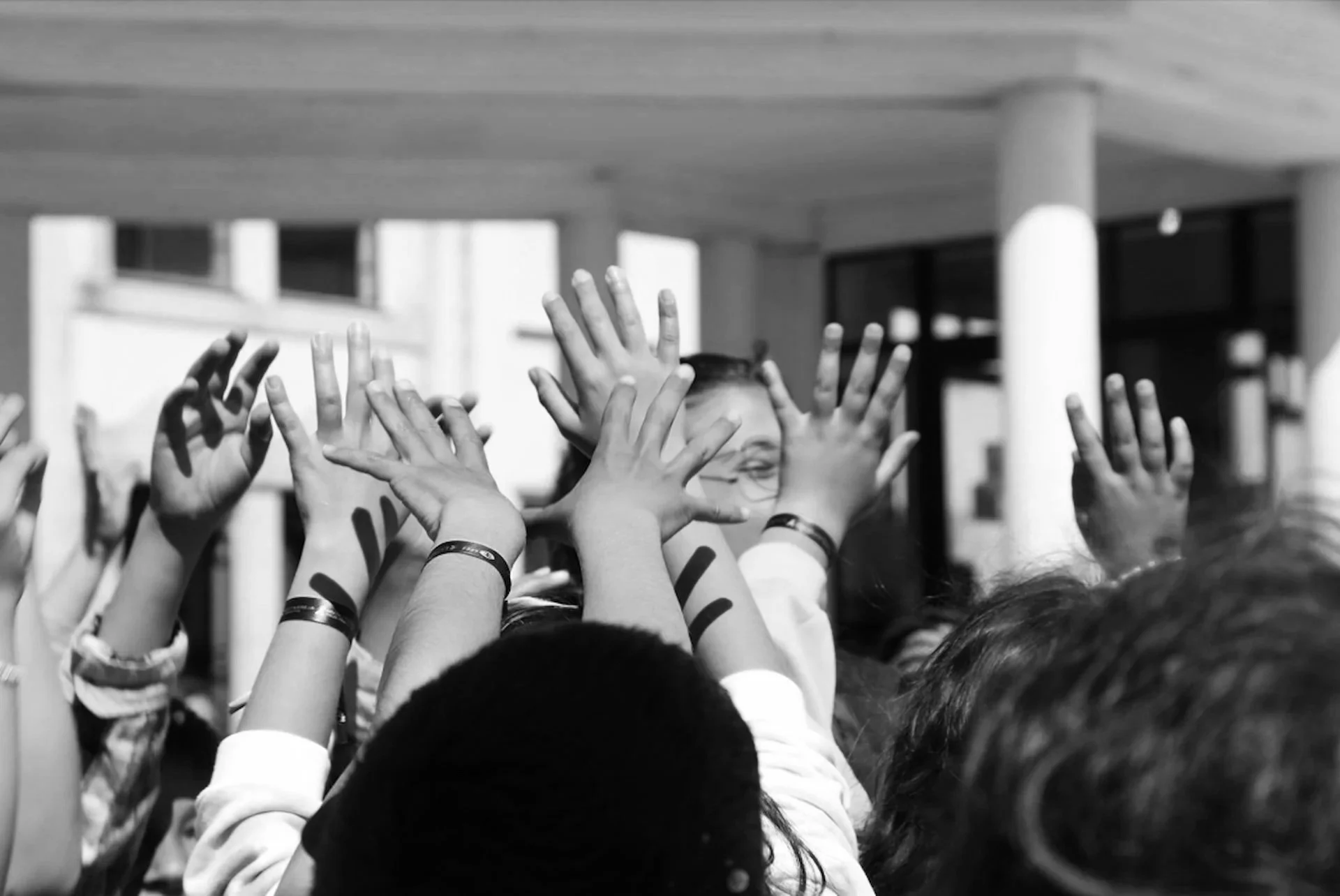 A group of children with raised hands reaching towards the front in a classroom or school setting.
