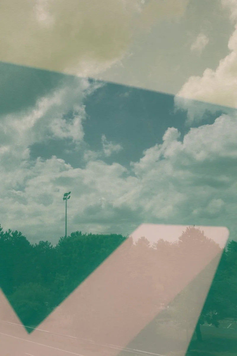 Reflet d'un ciel partiellement nuageux avec des arbres et un lampadaire dans une surface vitrée.