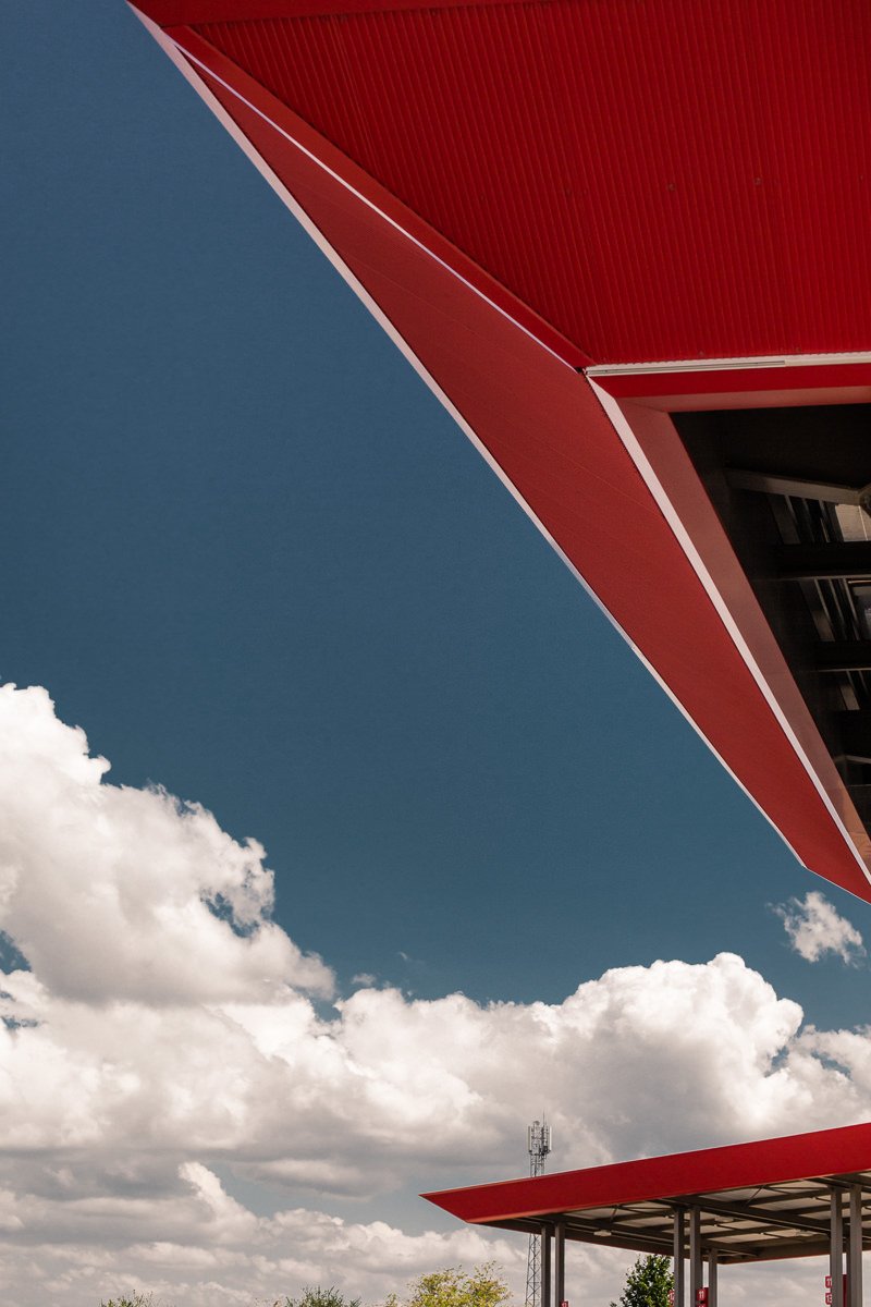 Vue de dessous d'un bâtiment moderne avec une façade rouge et un ciel nuageux en arrière-plan.