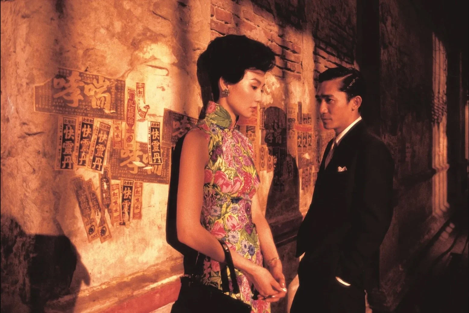 In the mood for love Un homme et une femme se regardant intensément dans une rue sombre, arrière-plan avec affiches en chinois.