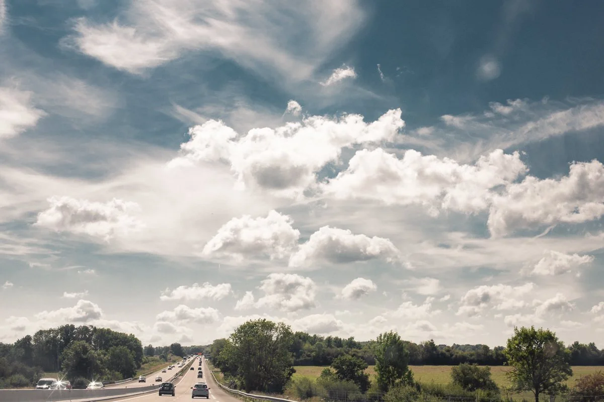 Une route avec des voitures sous un ciel nuageux avec quelques arbres et champs à côté.