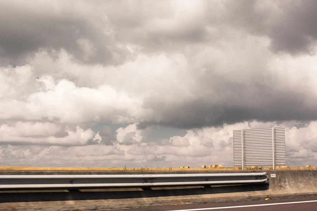 Vue d'une route avec une barrière de sécurité, des nuages gris dans le ciel et un panneau de signalisation en métal vide.