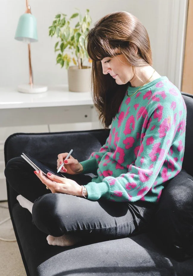 female artist sat on sofa crossed legged drawing on an ipad