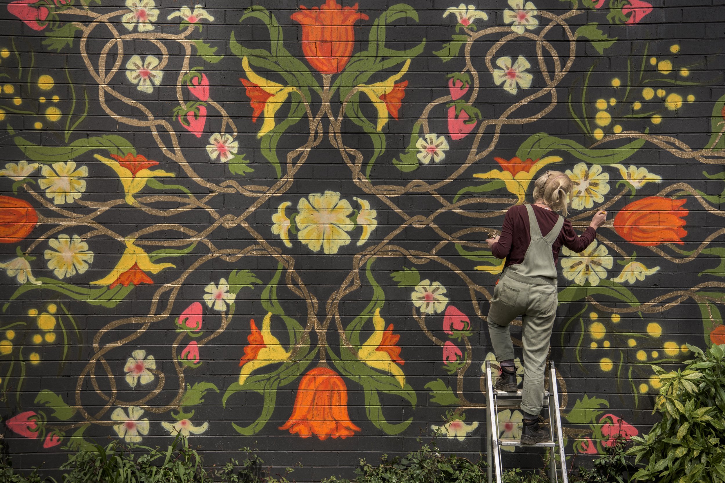 Elizabeth in her dungarees, on a ladder painting a mural. Photo by Mark Fergus