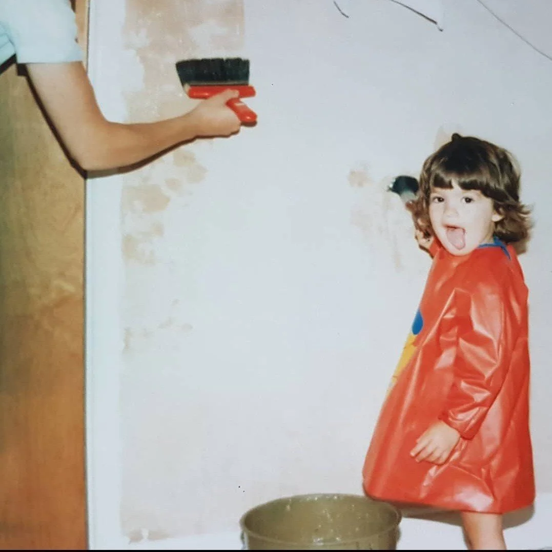 Young toddler girl painting the walls with her mum wearing an apron