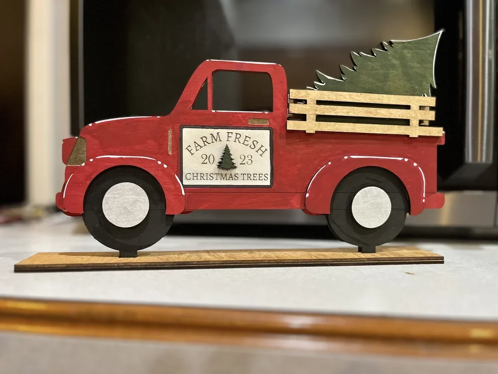 Wooden vintage farm truck figurine with Christmas Trees engraved on the door and laying in the truck bed