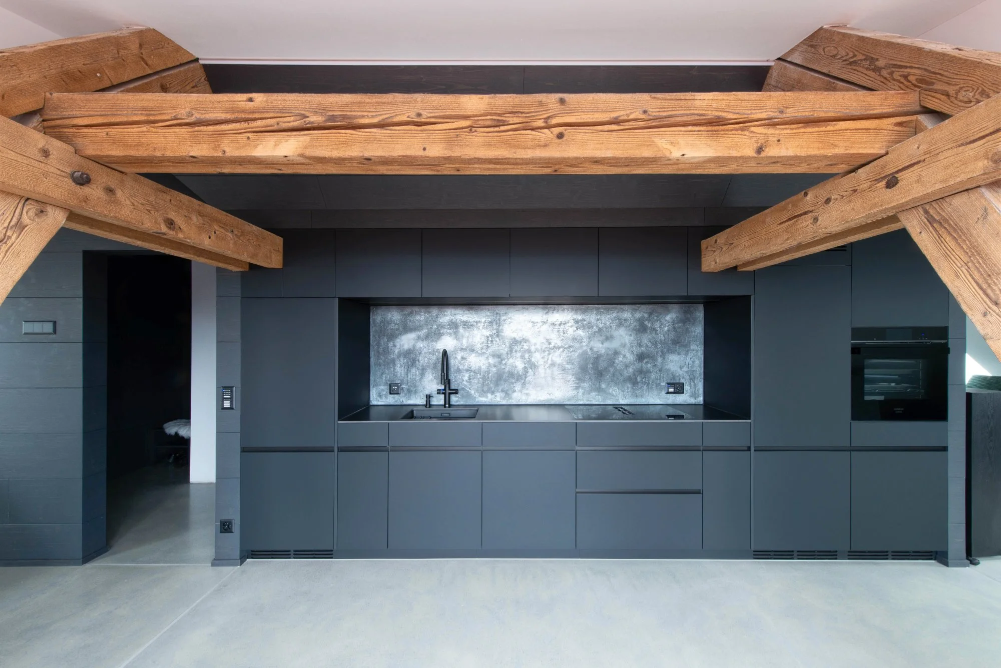 Moderne schwarze Küchenzeile mit schwarzem Backofen, schwarzem Herd, schwarzen Schränken, mit einem schwarzen Wasserhahn in einem Küchenraum mit Holzdecke und sichtbaren Holzbalken.