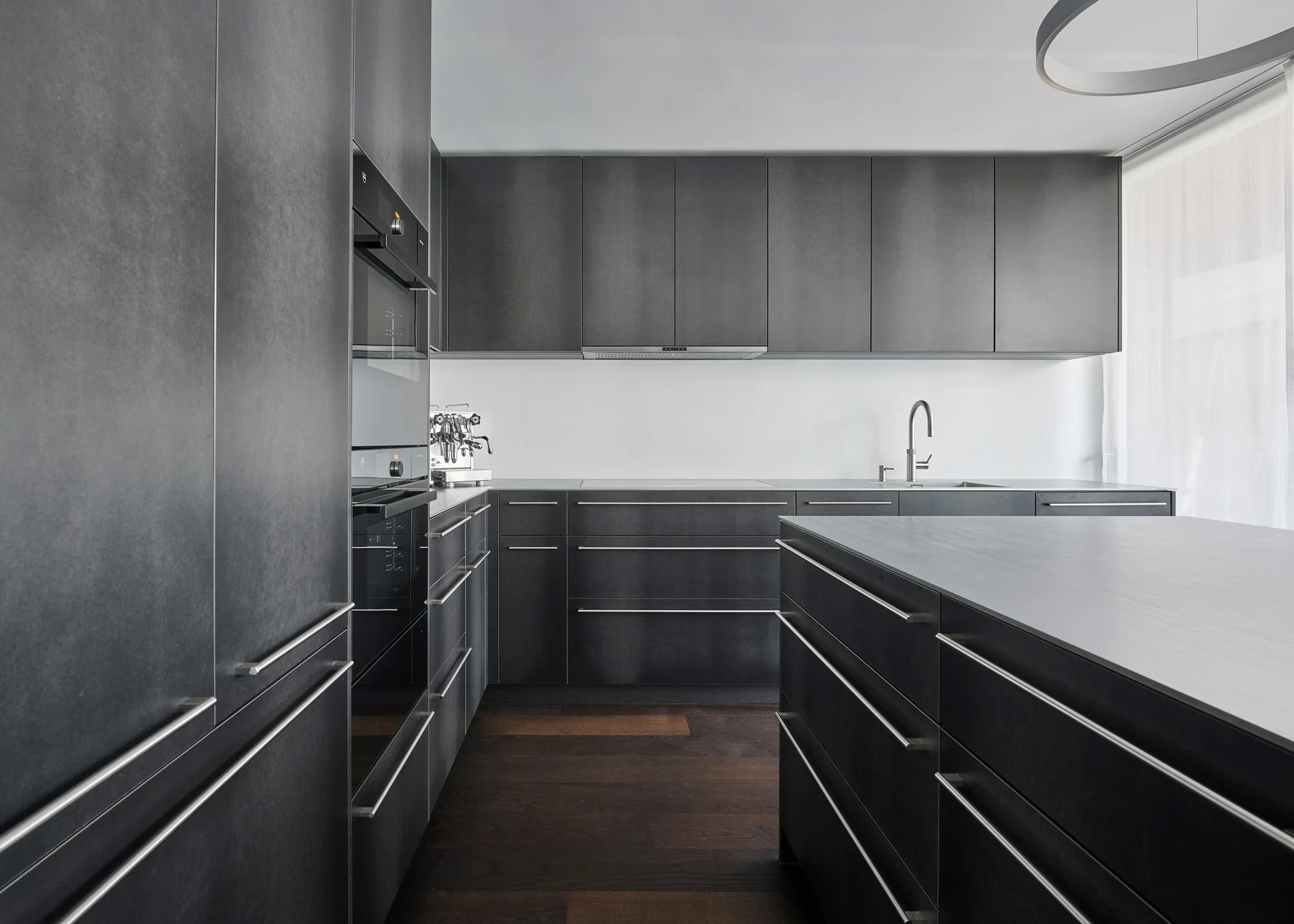 Moderne schwarze Küche mit dunklen Schränken, Holzarbeitsplatten und Edelstahlgriffen, Beleuchtung durch großes Fenster.