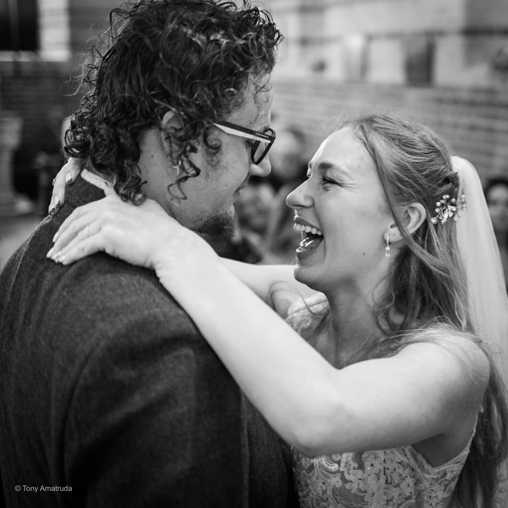 A man and a woman smiling and holding each other's faces close during a dance or intimate moment, with a blurred background.