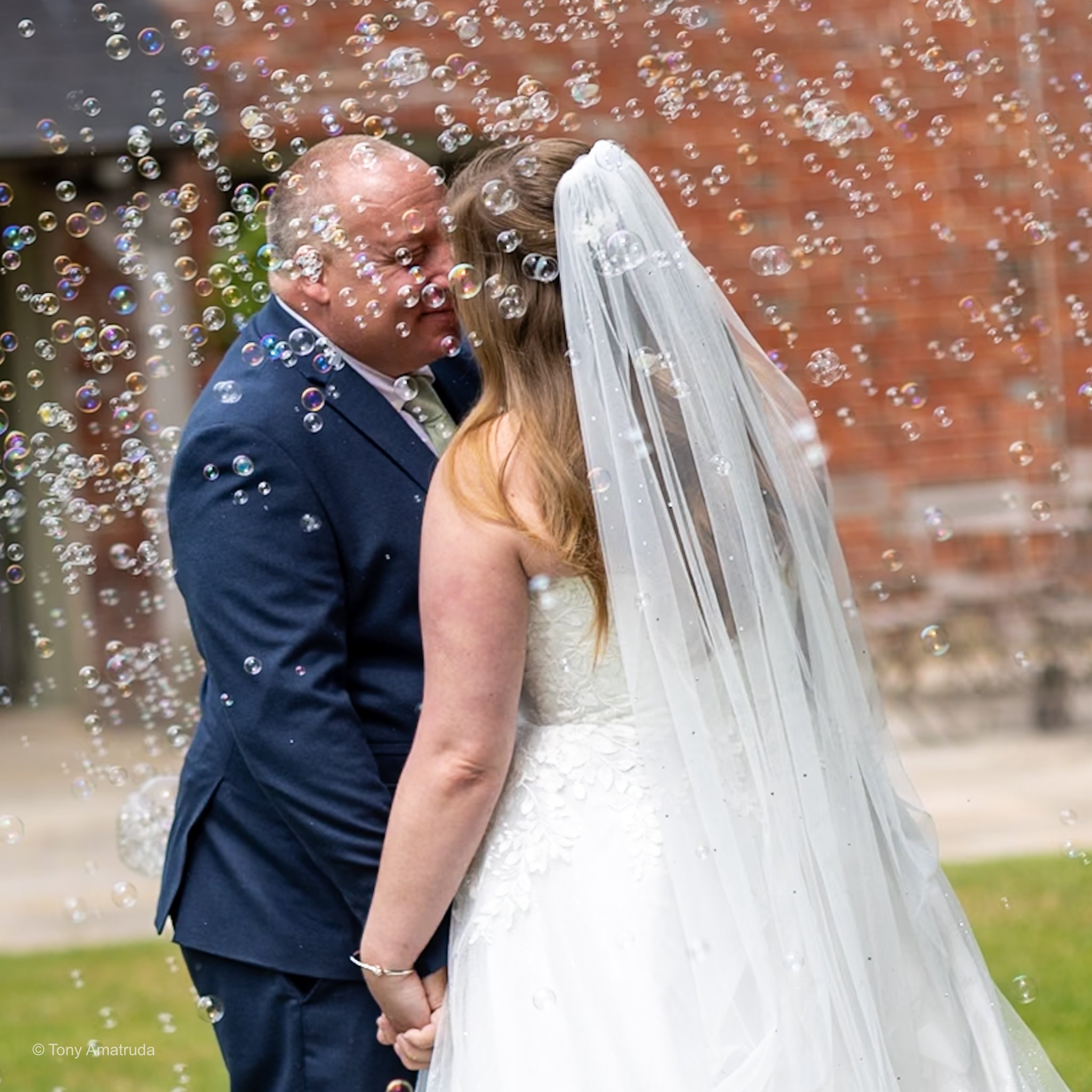 A bride and groom holding hands under a shower of bubbles during their wedding.