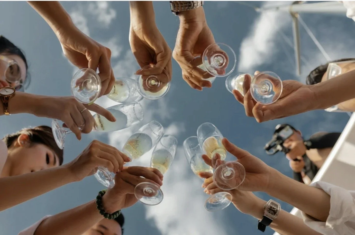 People toasting with glasses of champagne outdoors against a blue sky.