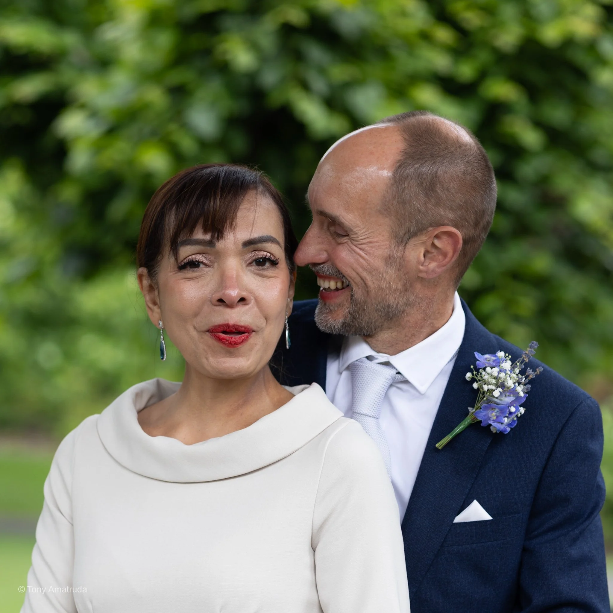 Close-up of a couple smiling and embracing each other outdoors, with a blurred green background.