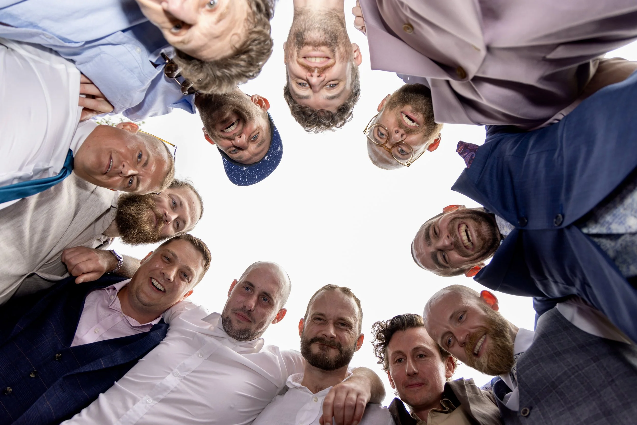 A group of men is standing in a circle, looking down at the camera and smiling.