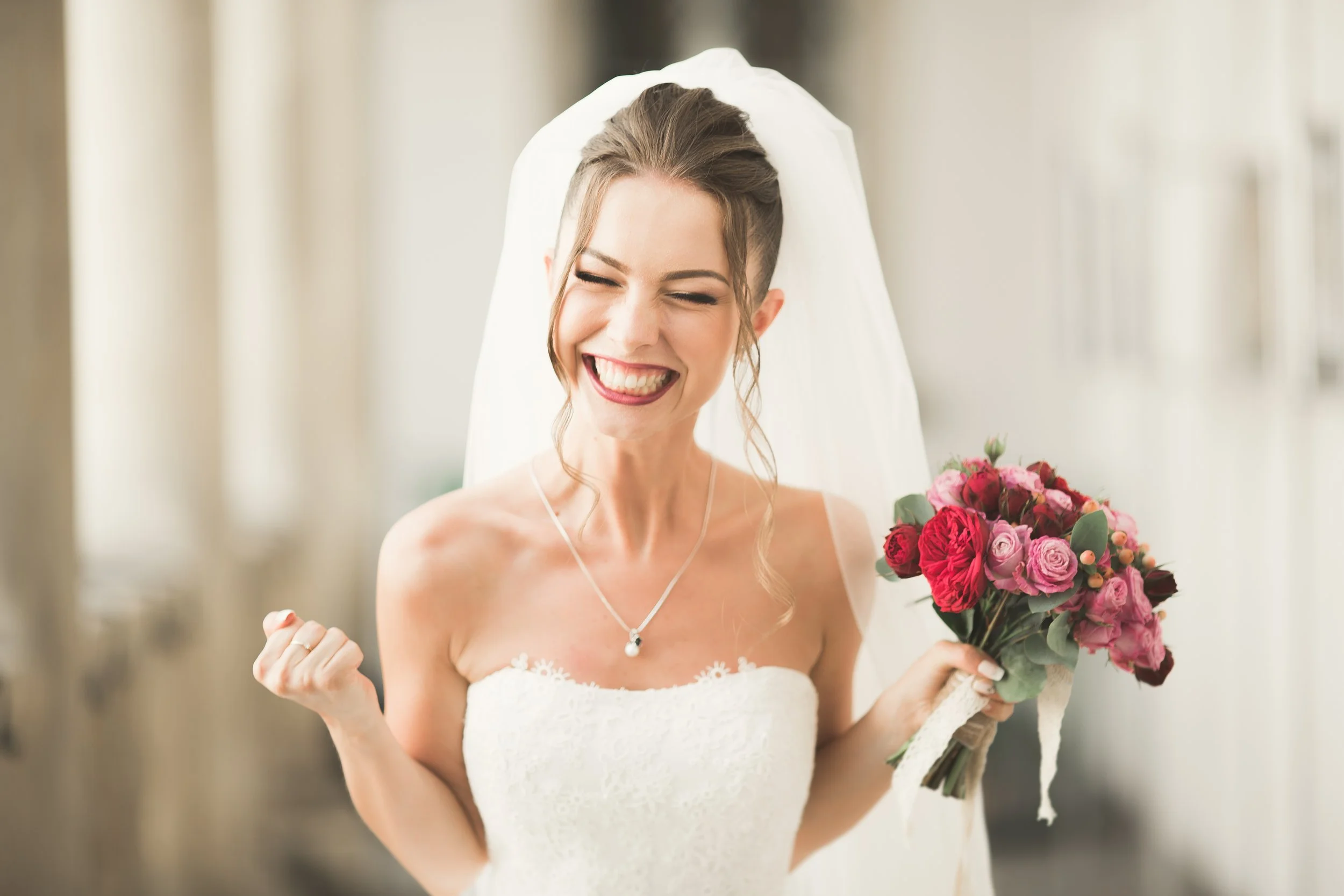 A smiling bride in a wedding dress holding a bouquet of pink and red flowers.