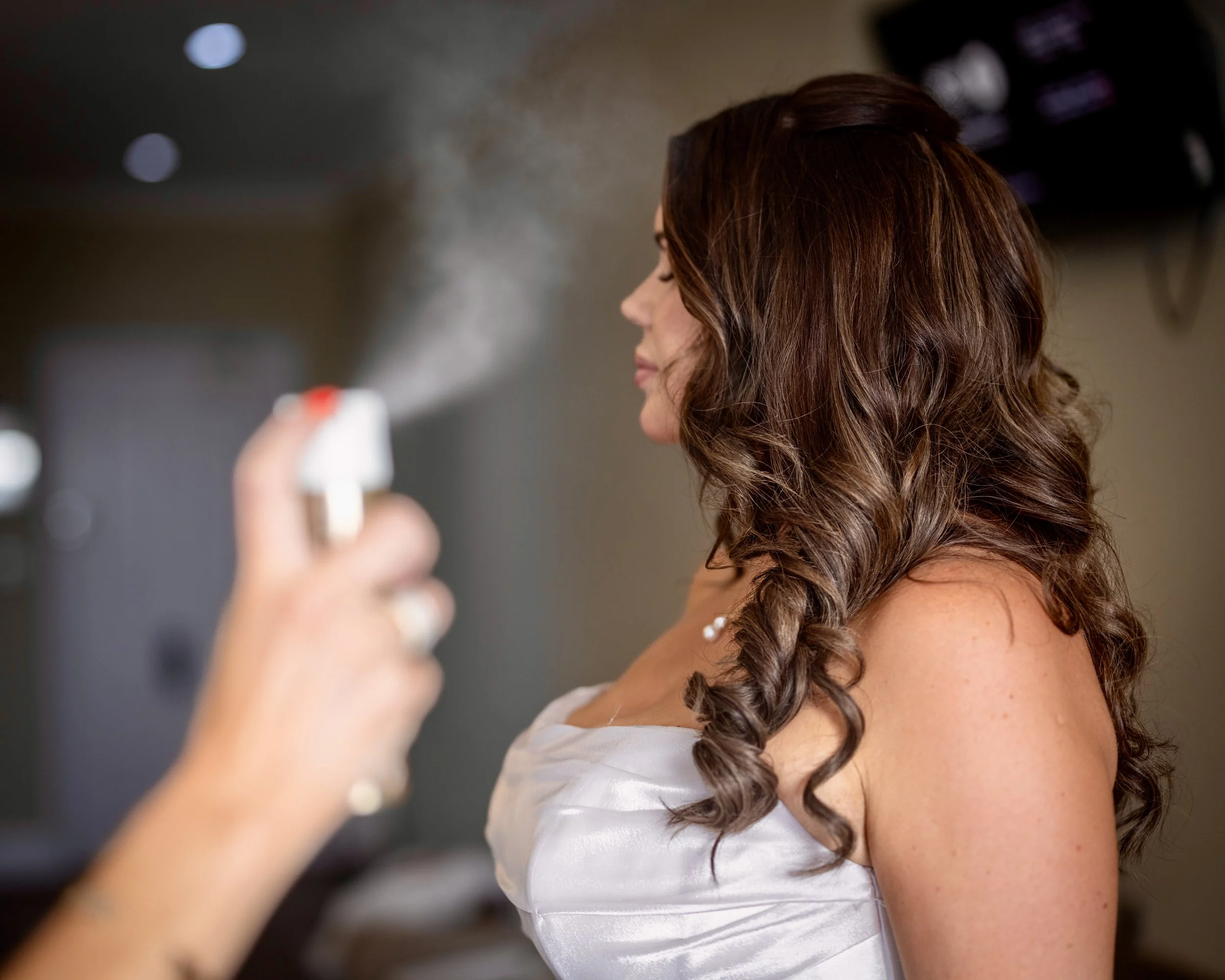 A woman with long, curly brown hair getting her hair sprayed at a beauty salon.