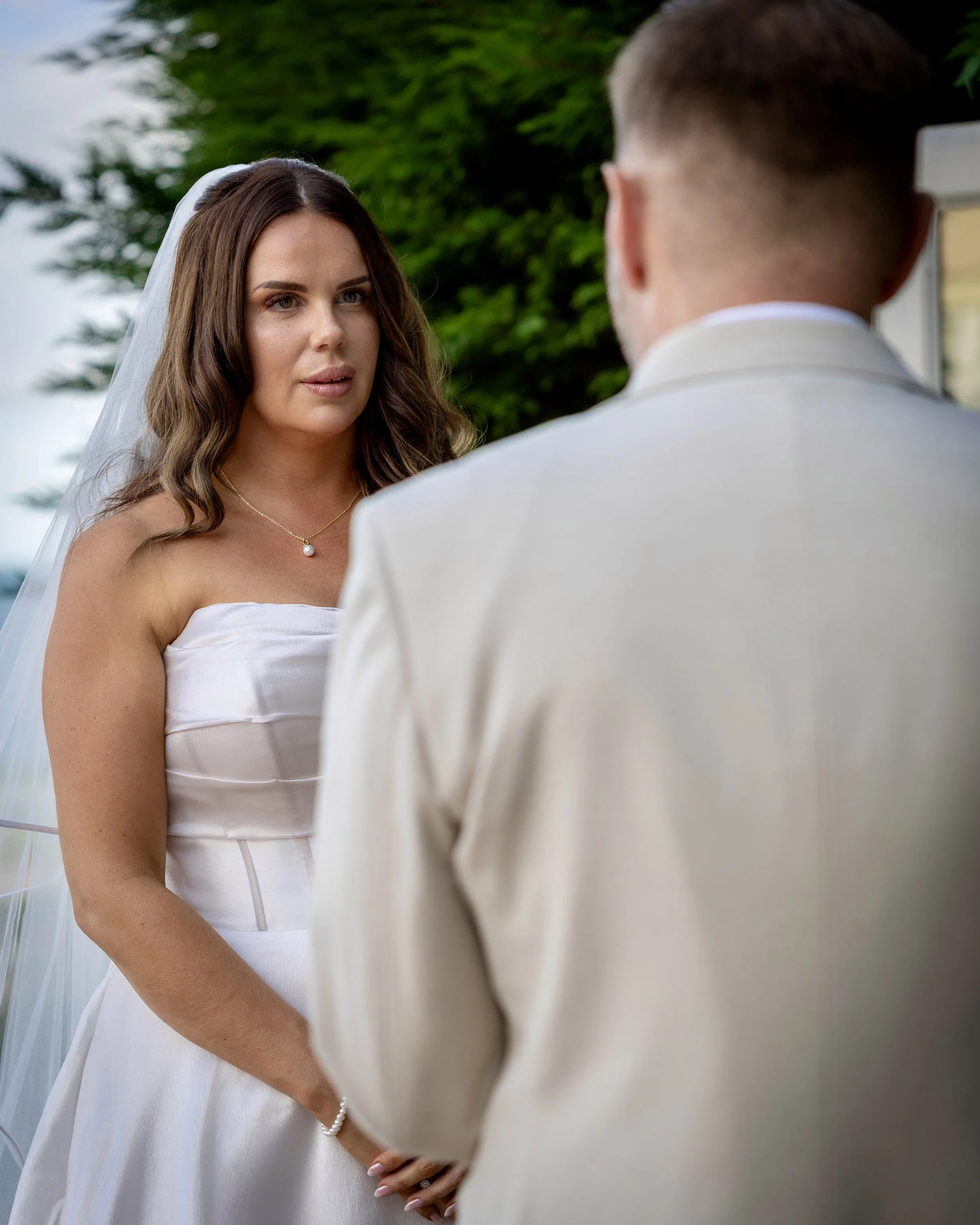 A bride and groom holding hands outdoors, with the bride looking at the groom.
