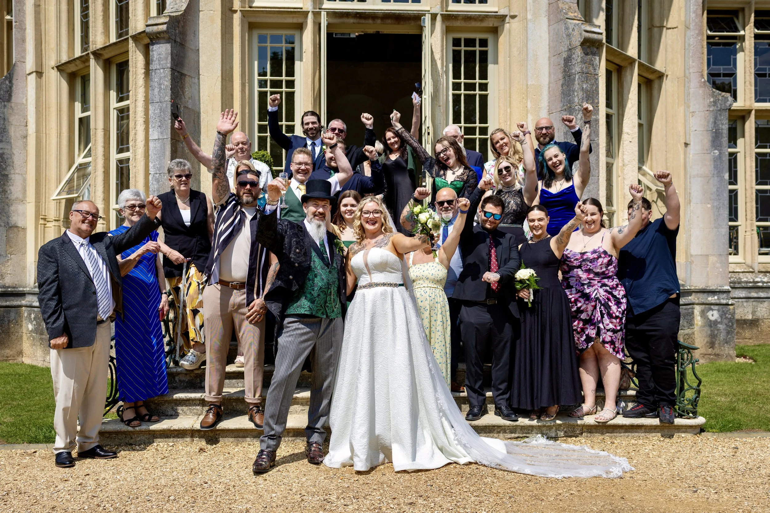 A group of people celebrating on the steps of a historic building, some with raised fists and smiling, with a woman in a white wedding dress in front.