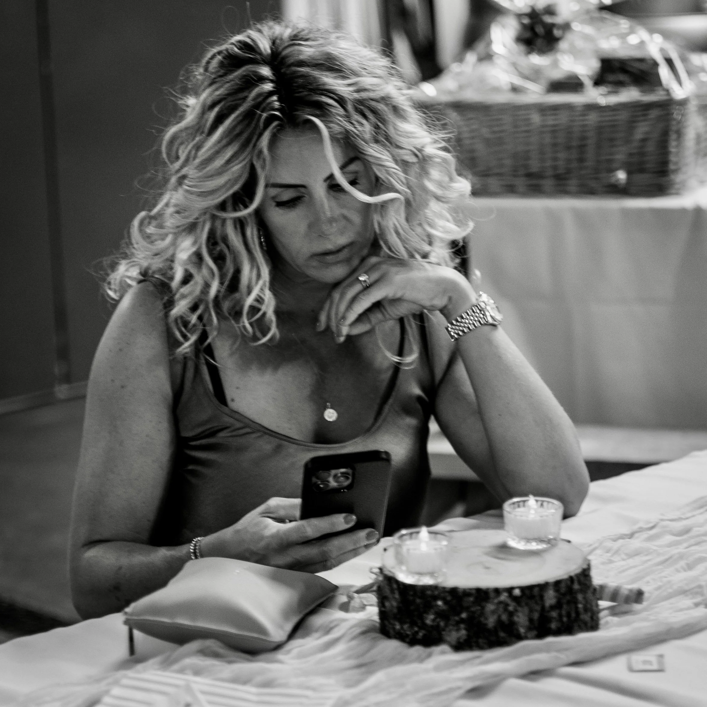 A woman with long, curly blonde hair is dining at a restaurant table, concentrating on her meal. She is wearing a bracelet and a necklace, and the table has plates and glasses with food and drinks.