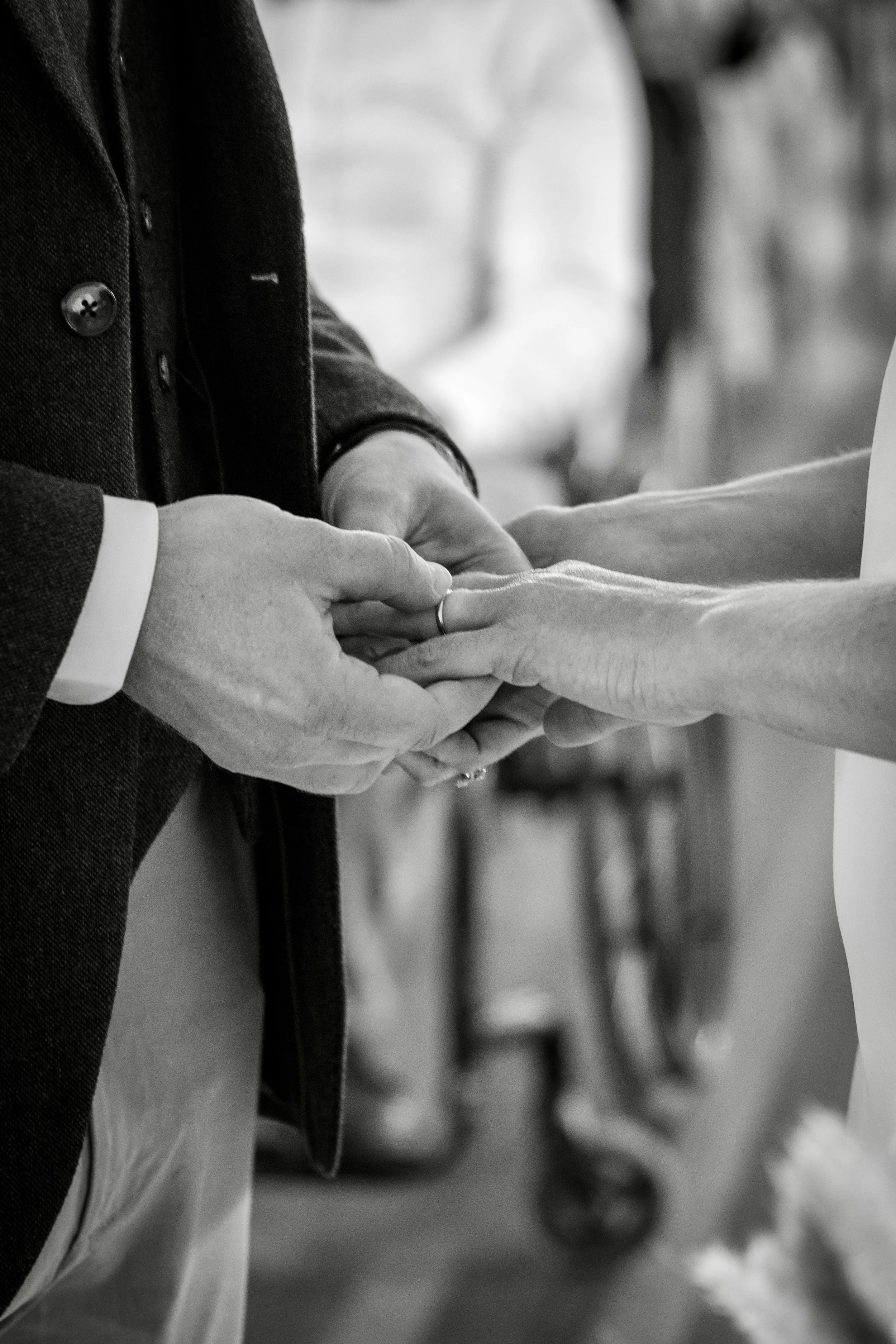 Close-up of two people exchanging rings, possibly during a wedding ceremony, with one person's hands placing a ring on the other's finger, in black and white.