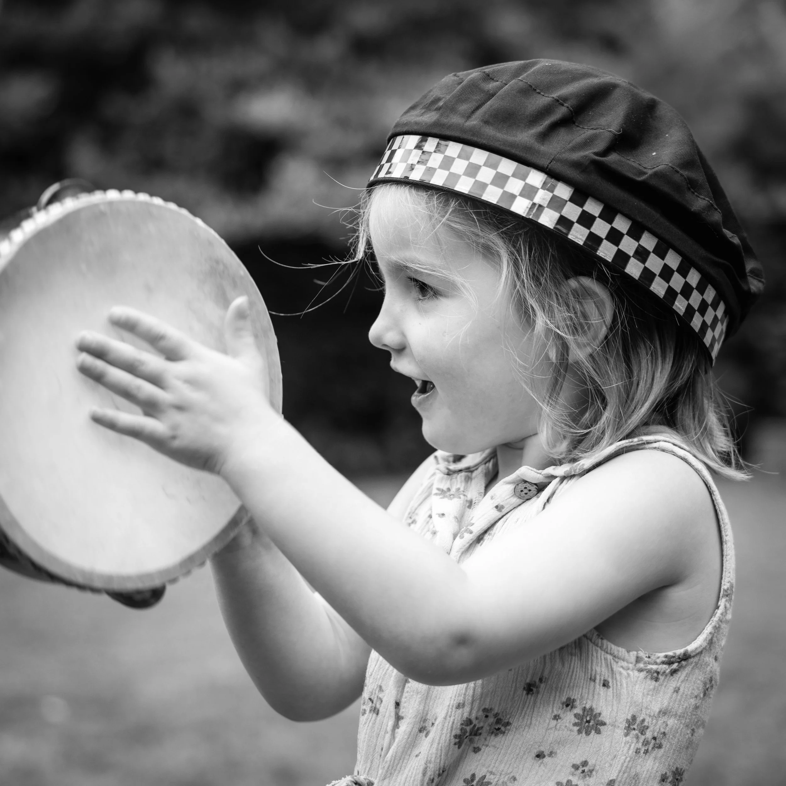 A young girl wearing a checkered headband and a floral patterned dress looks at a balloon.