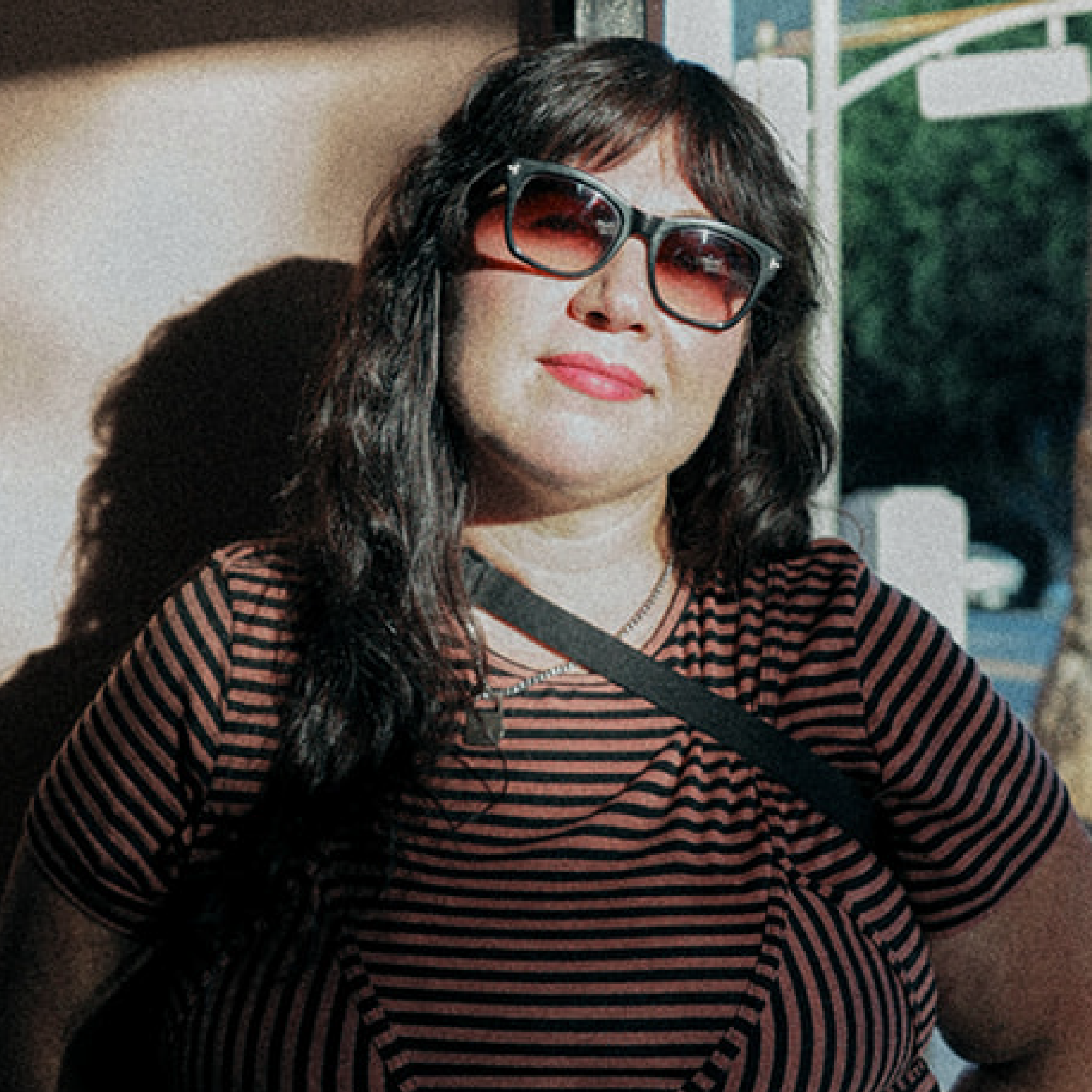 A person with long dark hair wears sunglasses and a striped shirt.