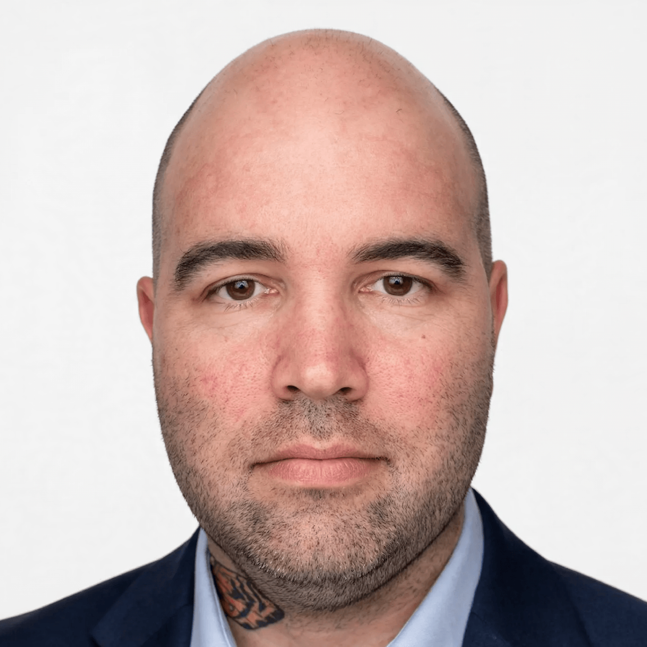 Caris, a bald person with a brown beard and neck tattoo, looks into the camera with a neutral and unsmiling expression.
