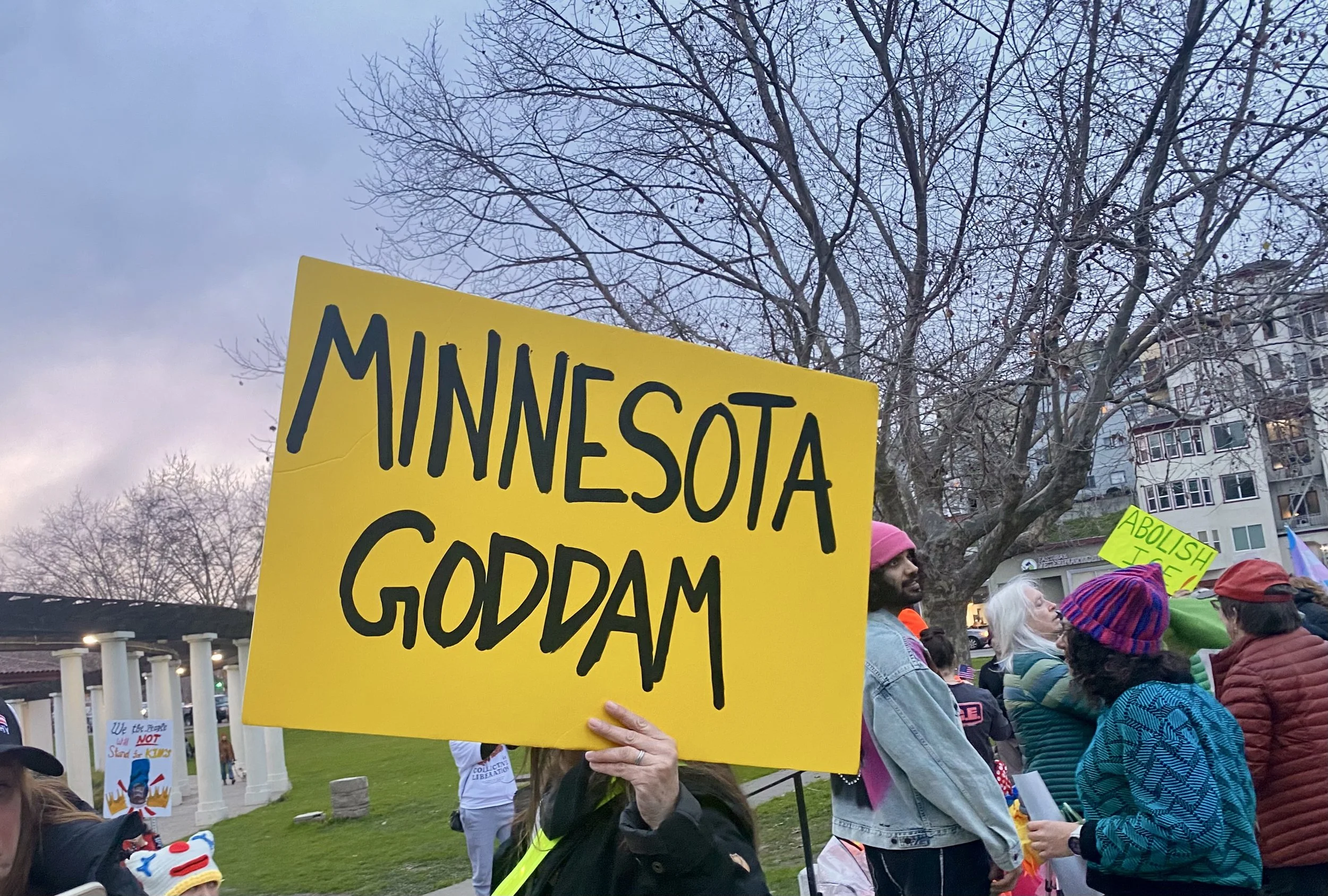 Yellow protest sign reading "Minnesota Goddam" surrounded by demonstrators at Lake Merritt