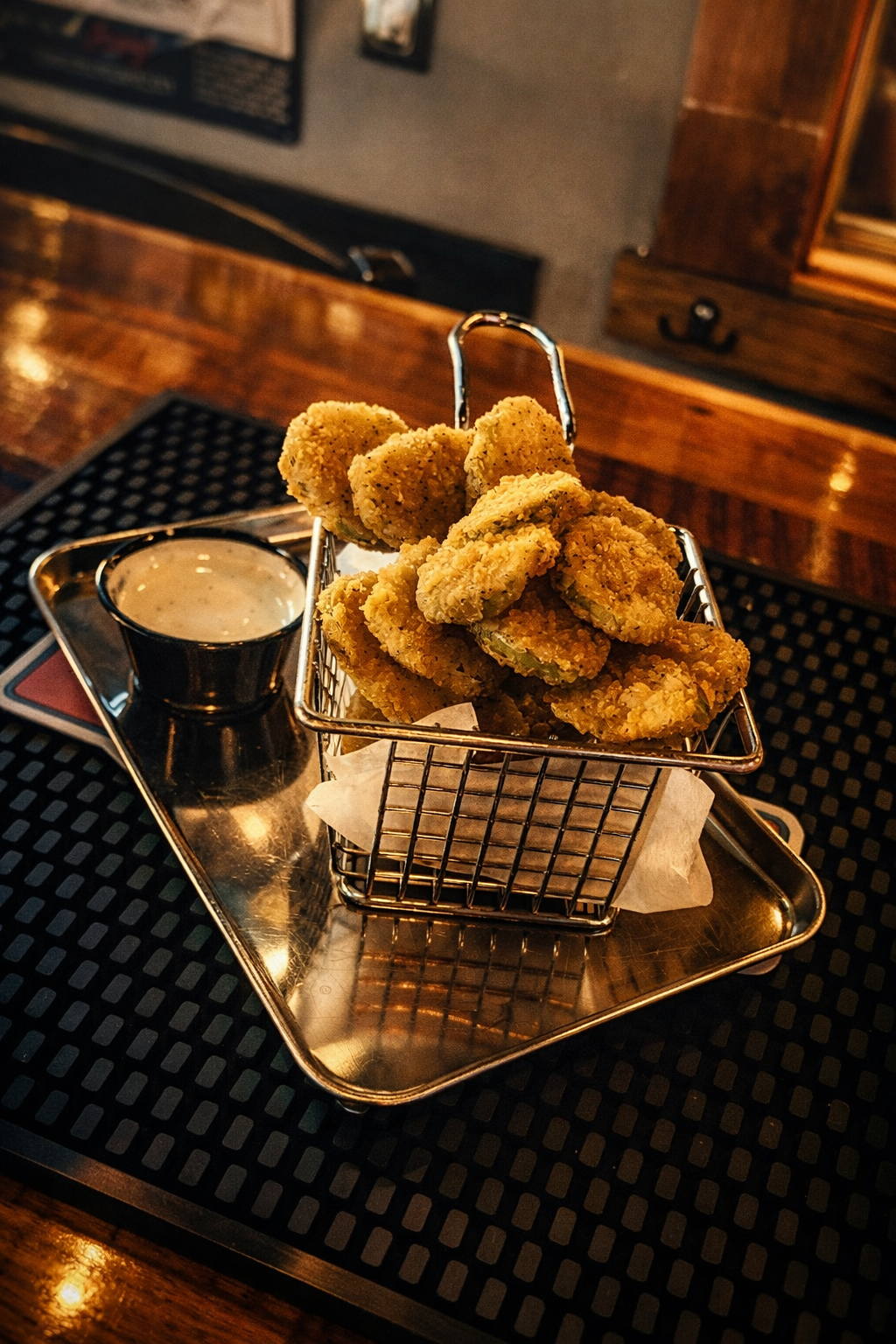 Basket of fried onion rings with a side of dipping sauce on a metal tray in a restaurant setting.