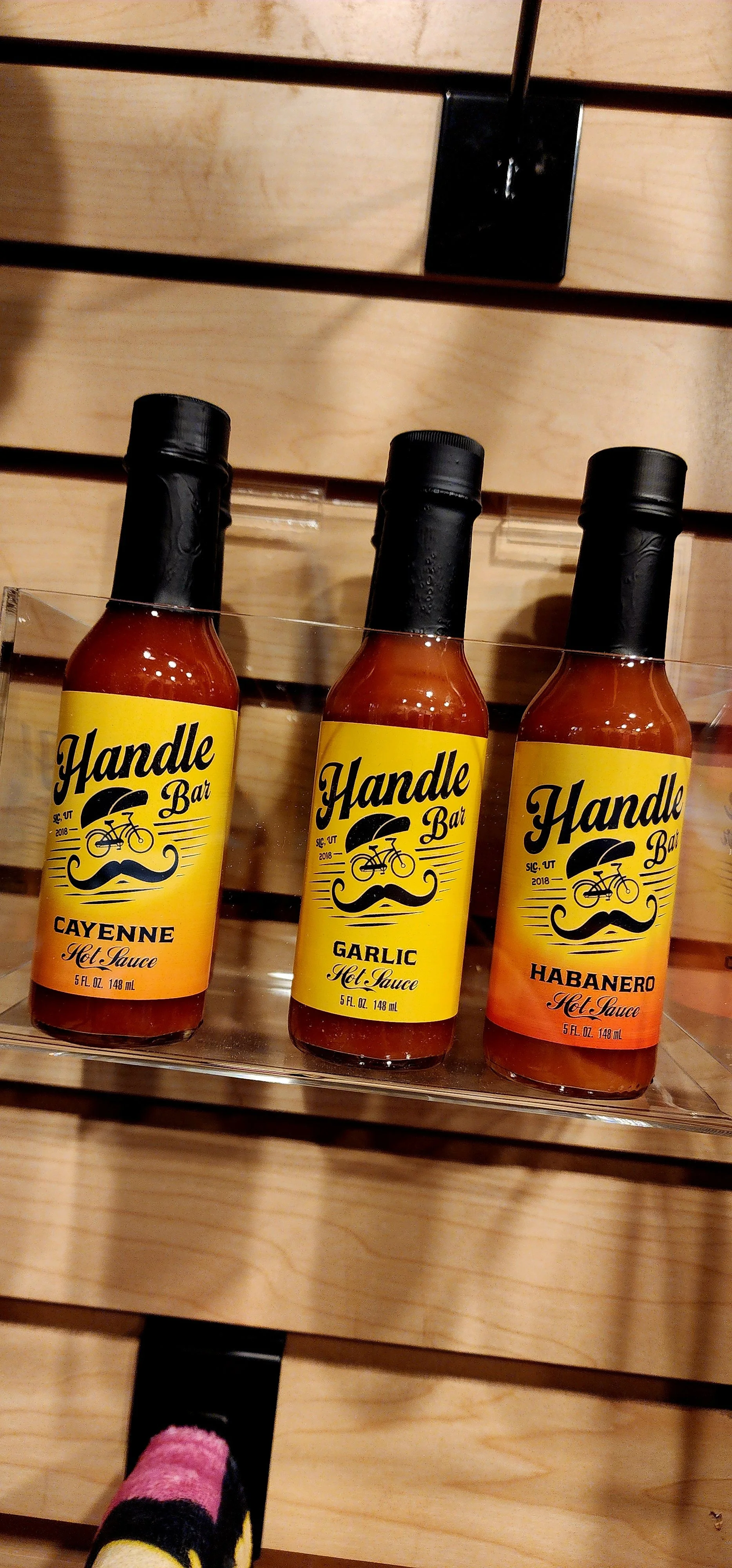 Three bottles of Handle Bar hot sauce labeled cayenne, garlic, and habanero, placed on a wooden display shelf.
