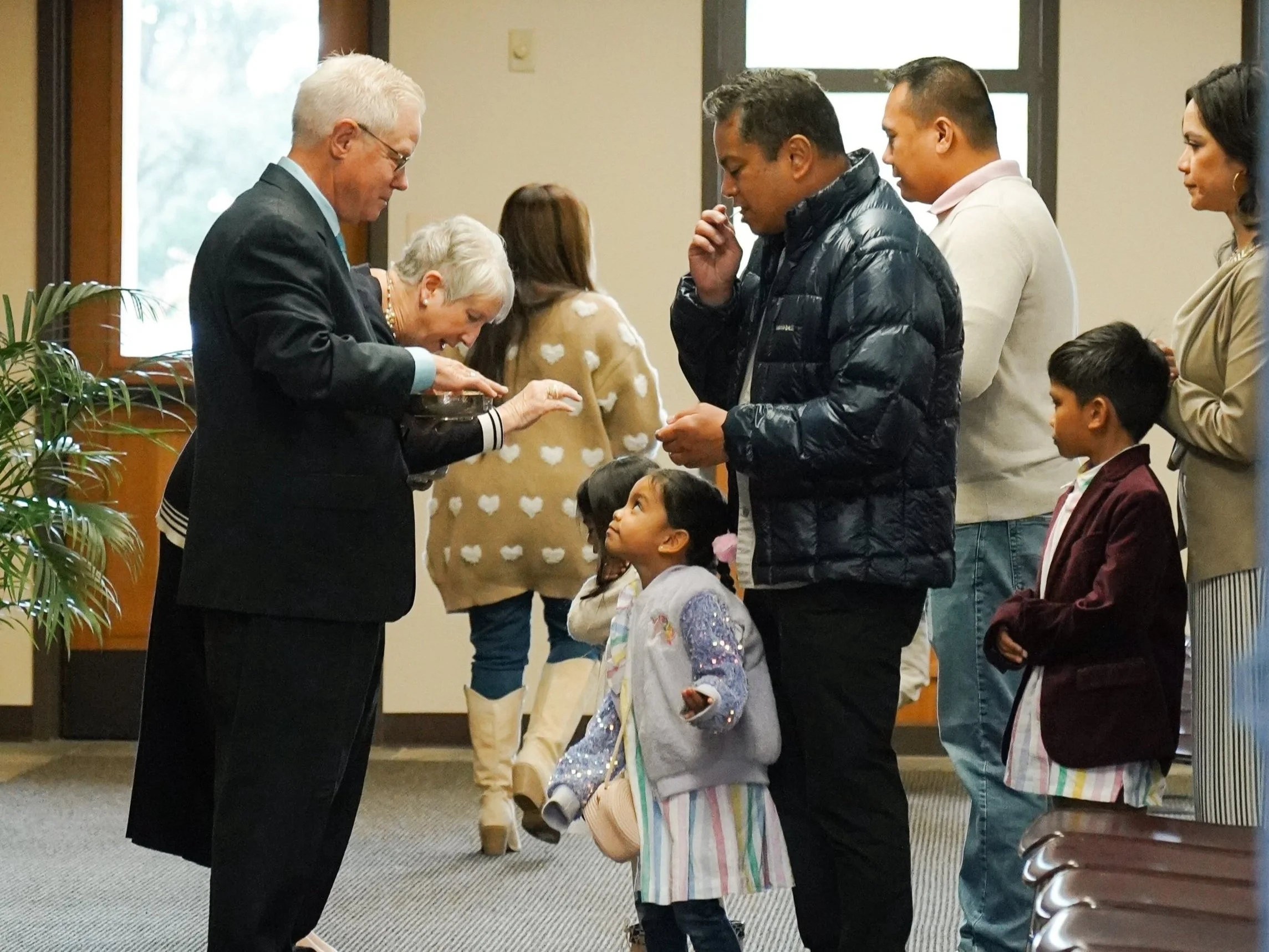 People in line at a religious or ceremonial event, with a young girl looking up at an older man.