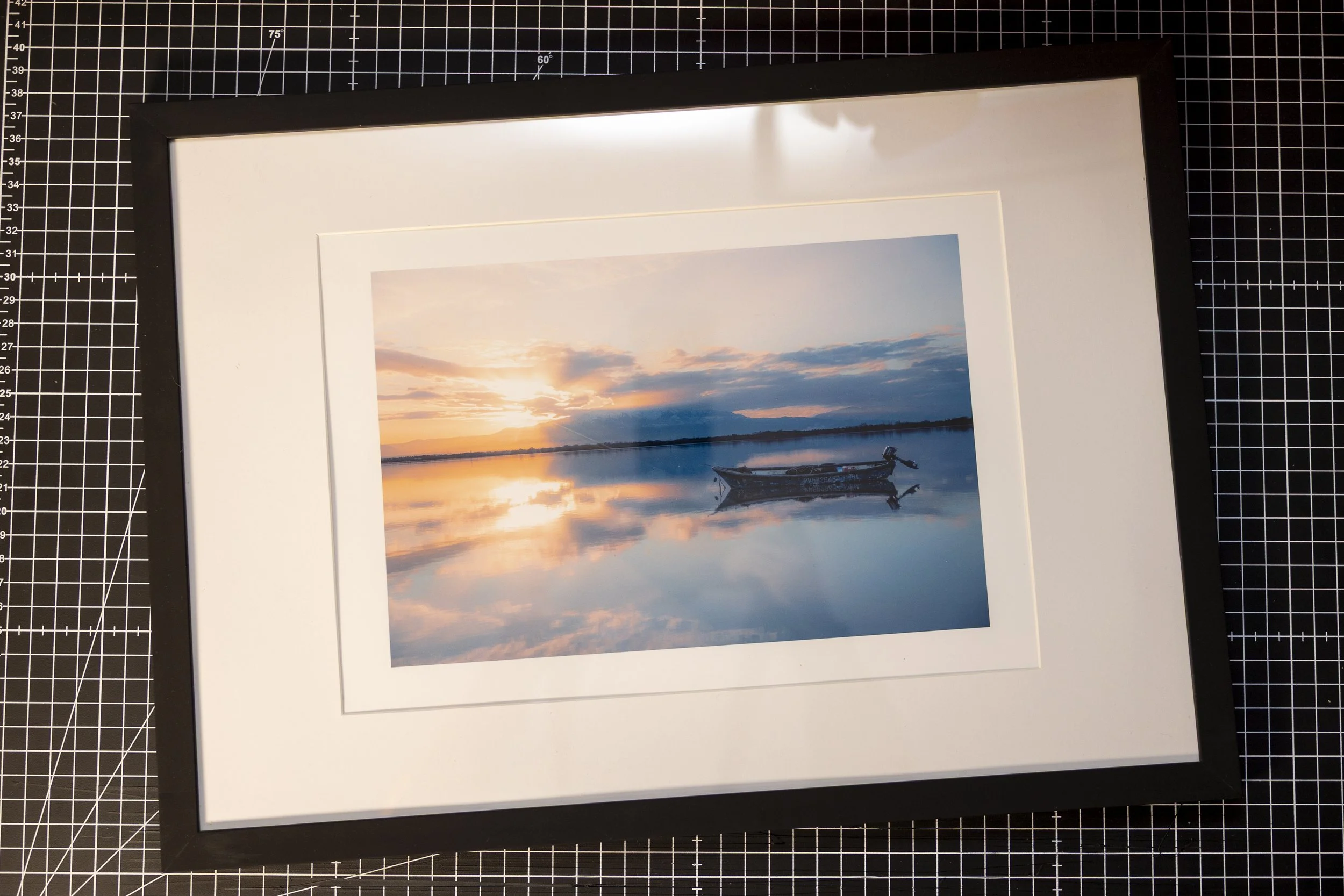 Photo d'un paysage avec un coucher de soleil, un lac calme et un bateau au centre, avec des nuages dans le ciel, reflet dans l'eau.