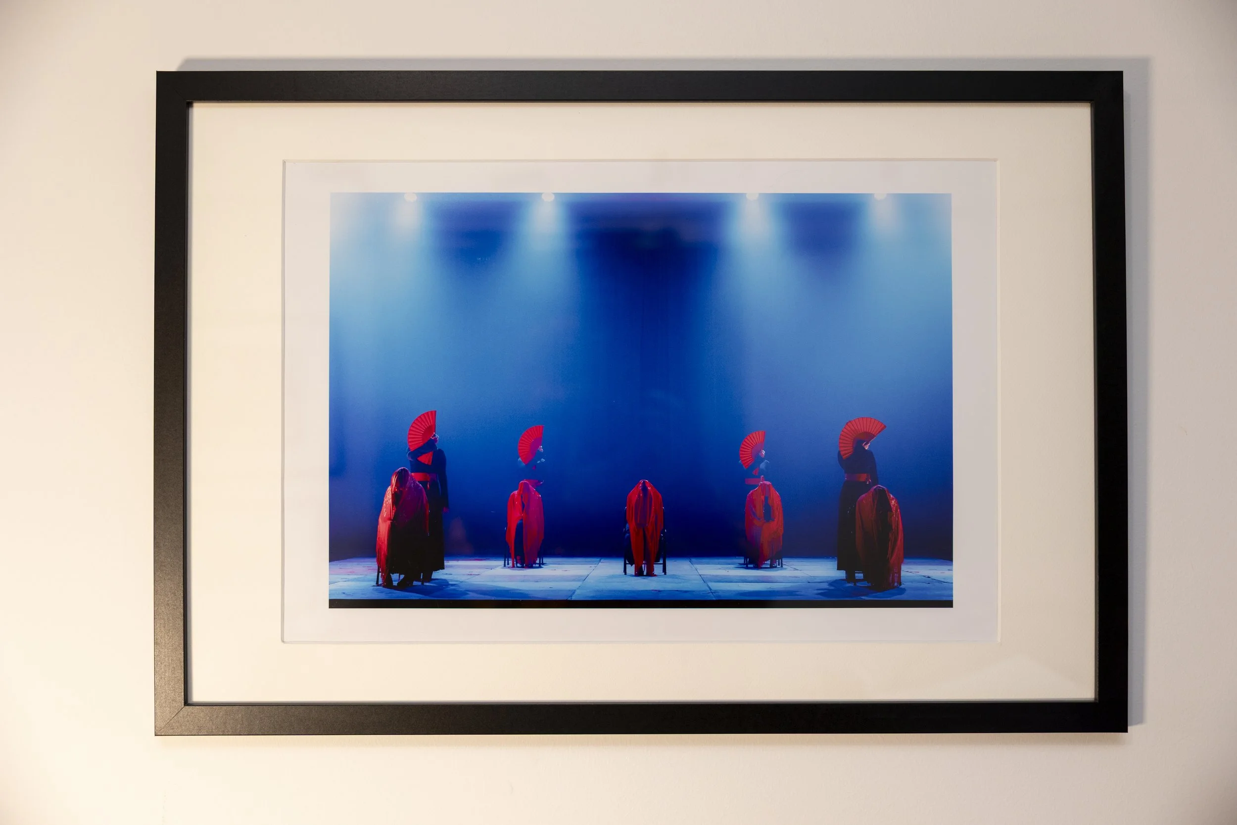 Une photographie représentant des danseurs traditionnels japonais portant des kimonos rouges et des éventails rouges, sur scène éclairée par des lumières bleues.