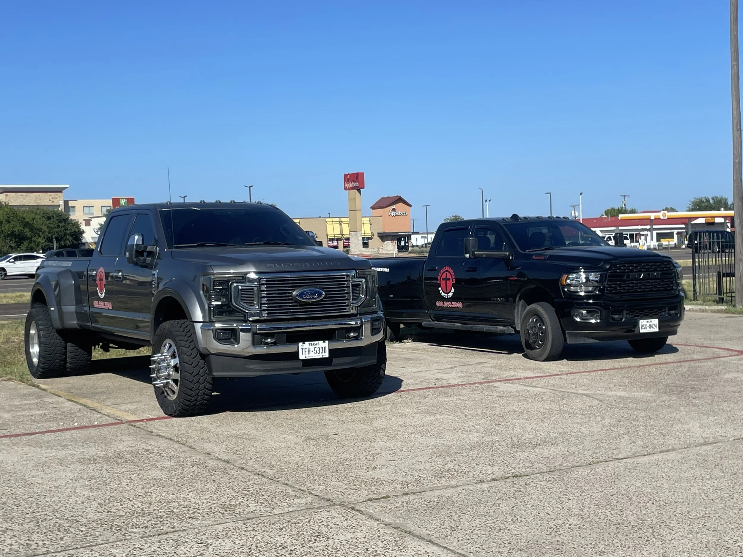 Pickup truck with custom tires and logo parked in a shopping center lot near Applebee's and other stores.