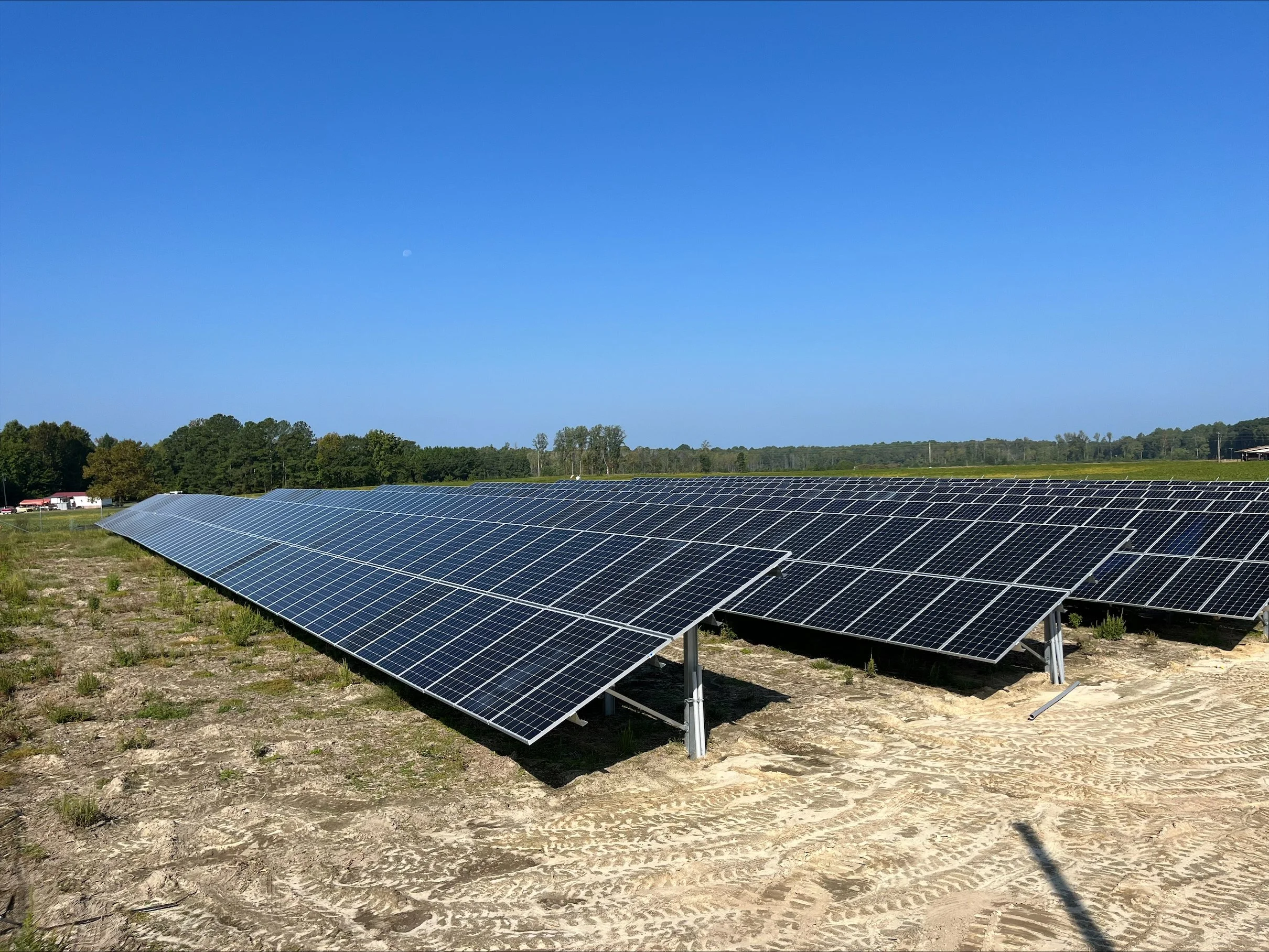 Multiple rows of solar panels installed on a dry, dusty field under a clear blue sky.